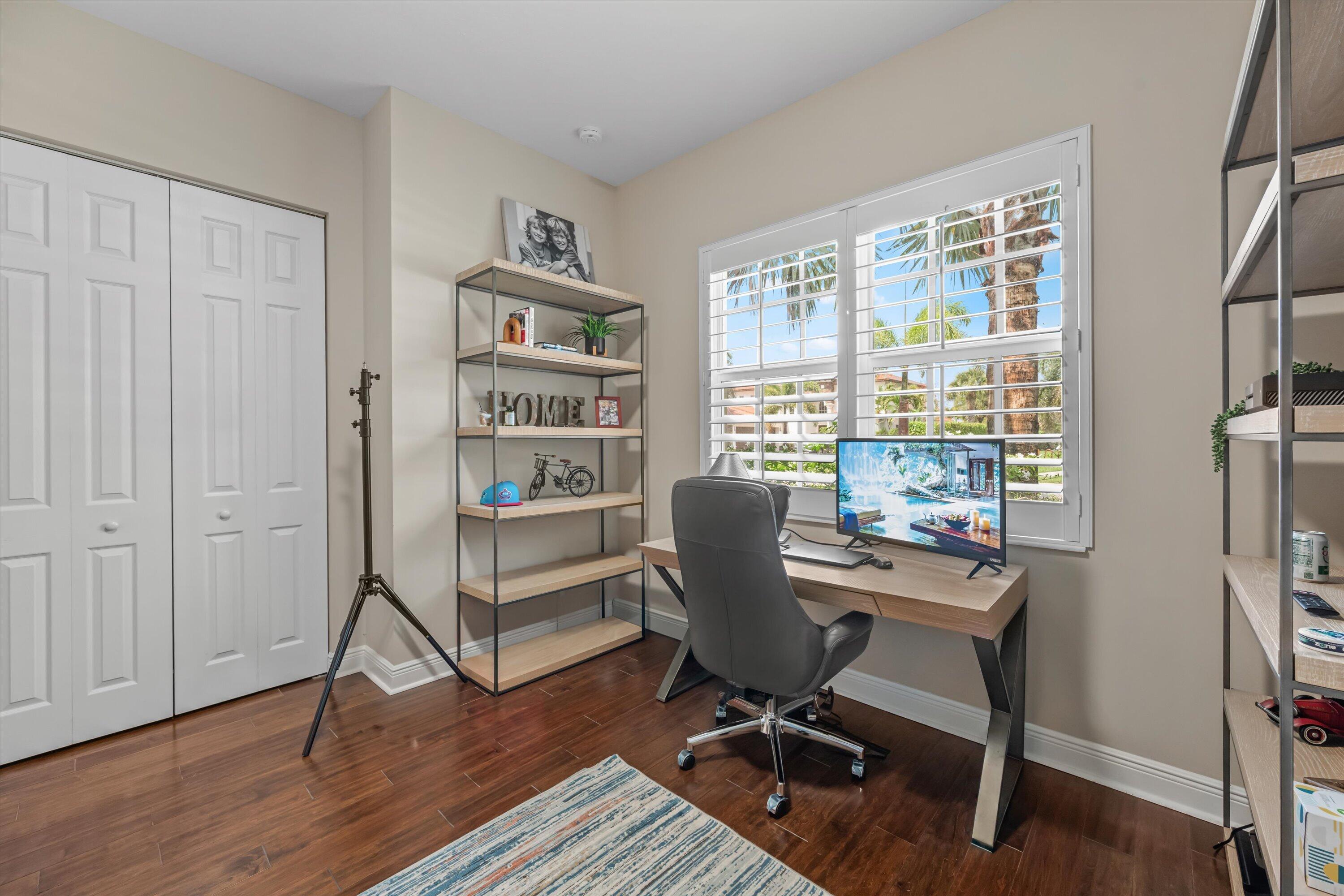 Home office with a wood desk, leather chair, plantation shutters, and white closet doors.