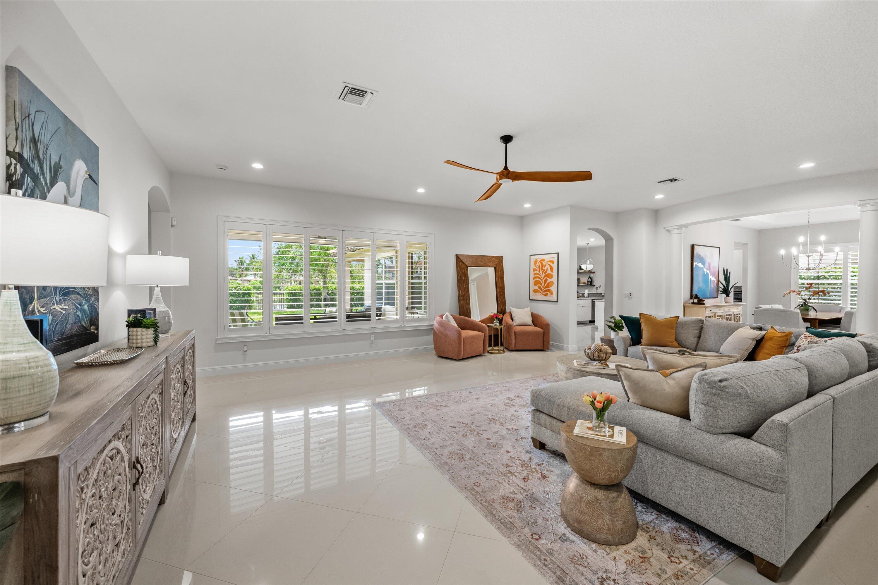 Furnished living room with a gray sectional, rust-colored armchairs, and shuttered windows overlooking greenery.