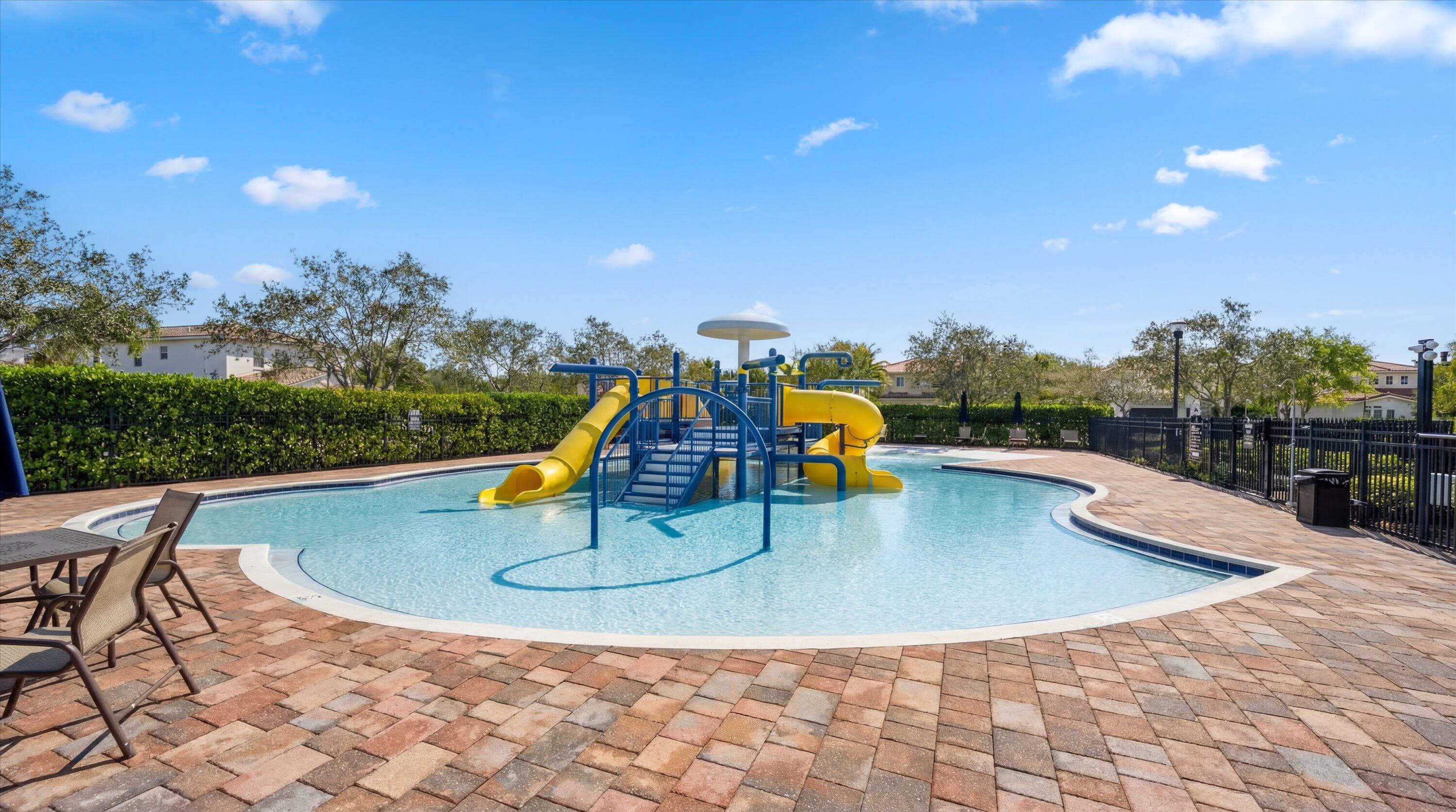 Community pool with a blue-and-yellow water-play structure and brick-paver deck.