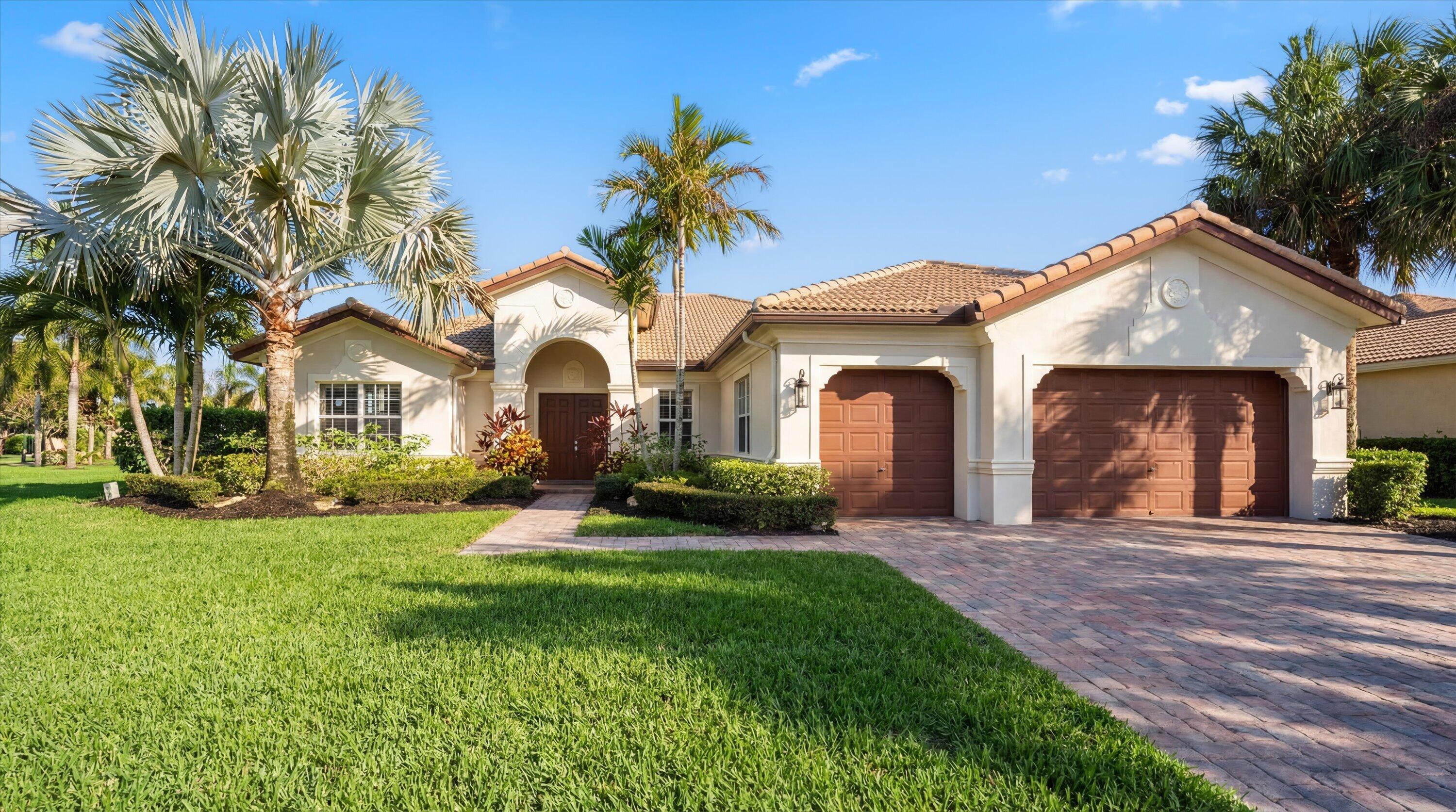 Cream stucco home with an arched entry, tile roof, palm trees, and a wide paver driveway.