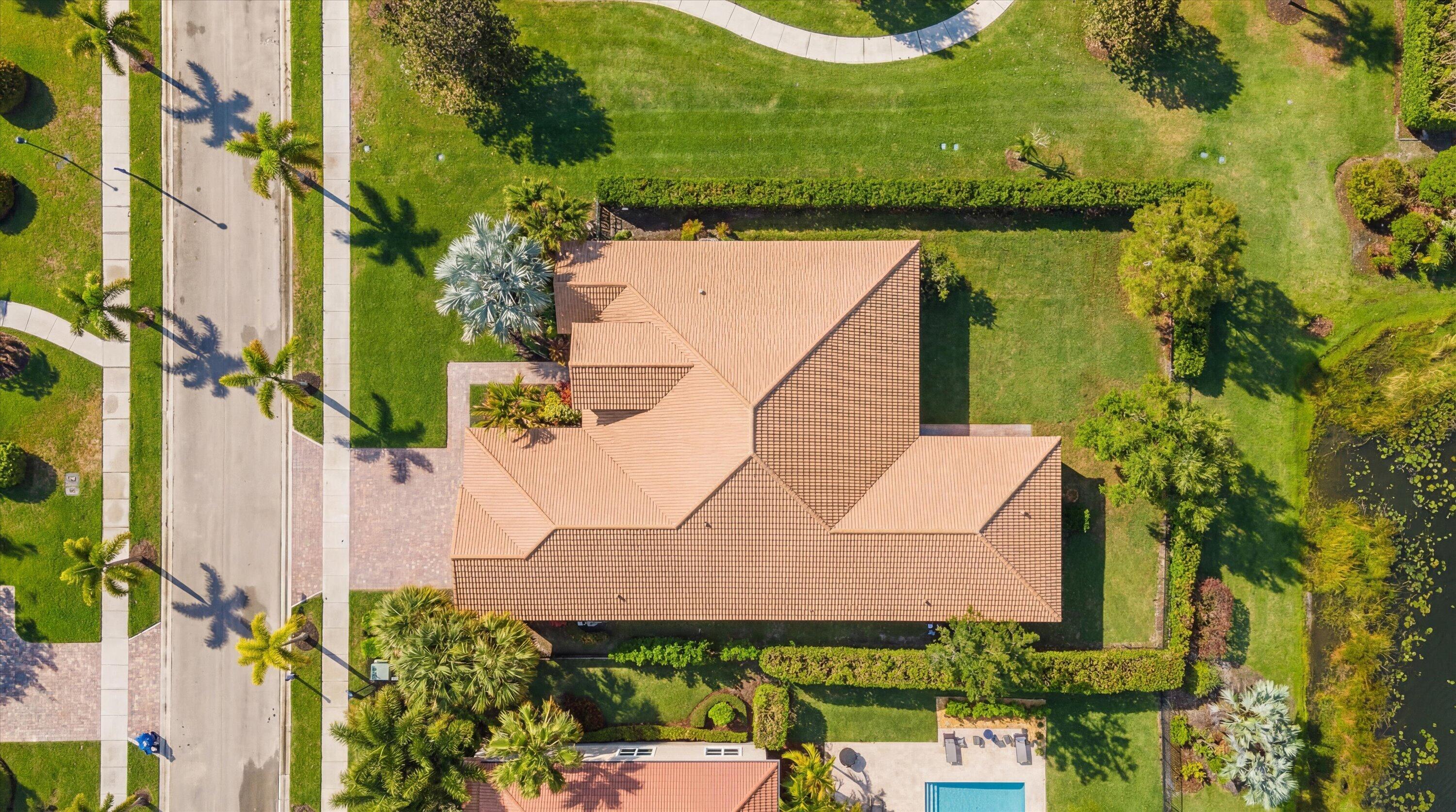 Aerial view of a terracotta-roofed home surrounded by palms and lawn beside a pond.