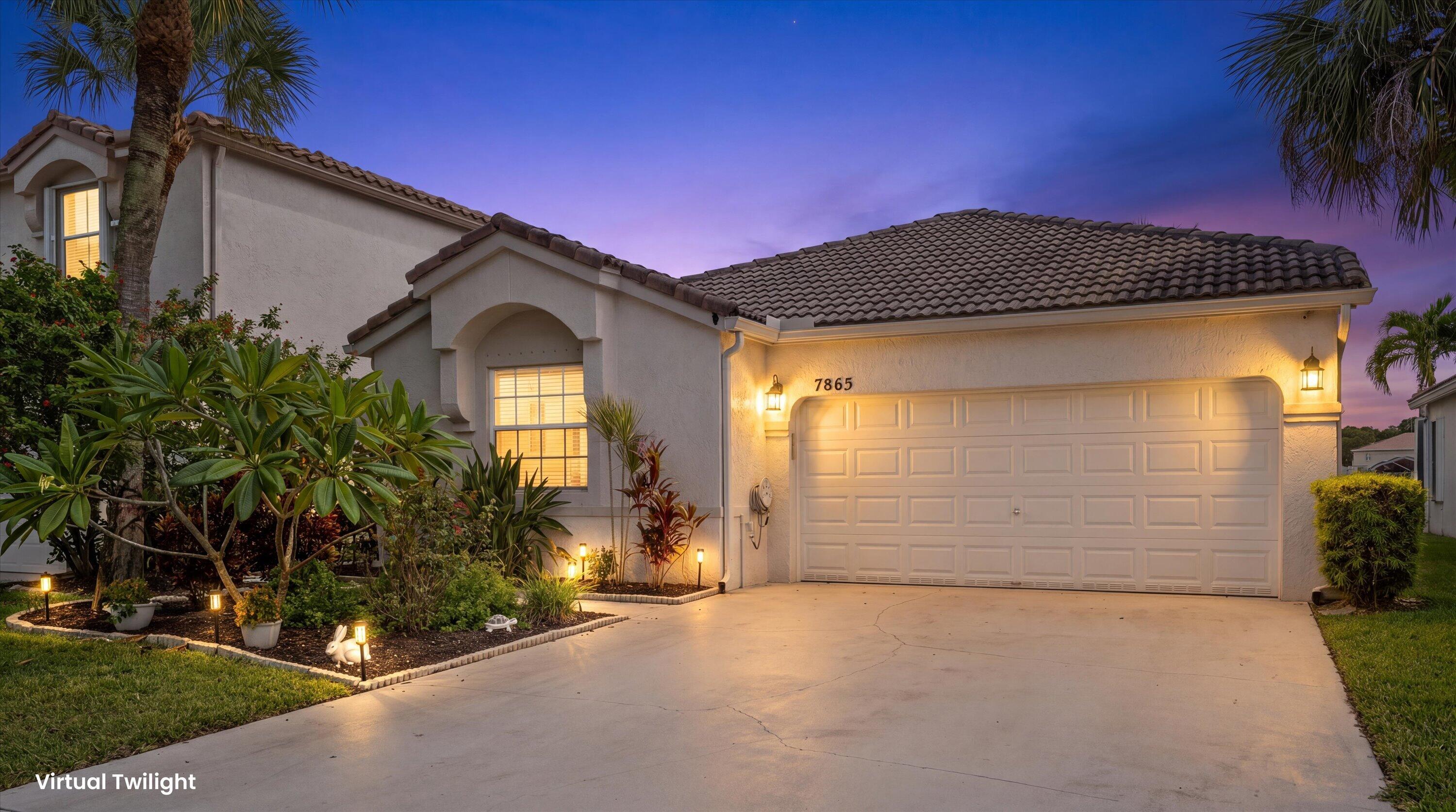 Stucco home with tiled roof, illuminated garage, and tropical landscaping at twilight.
