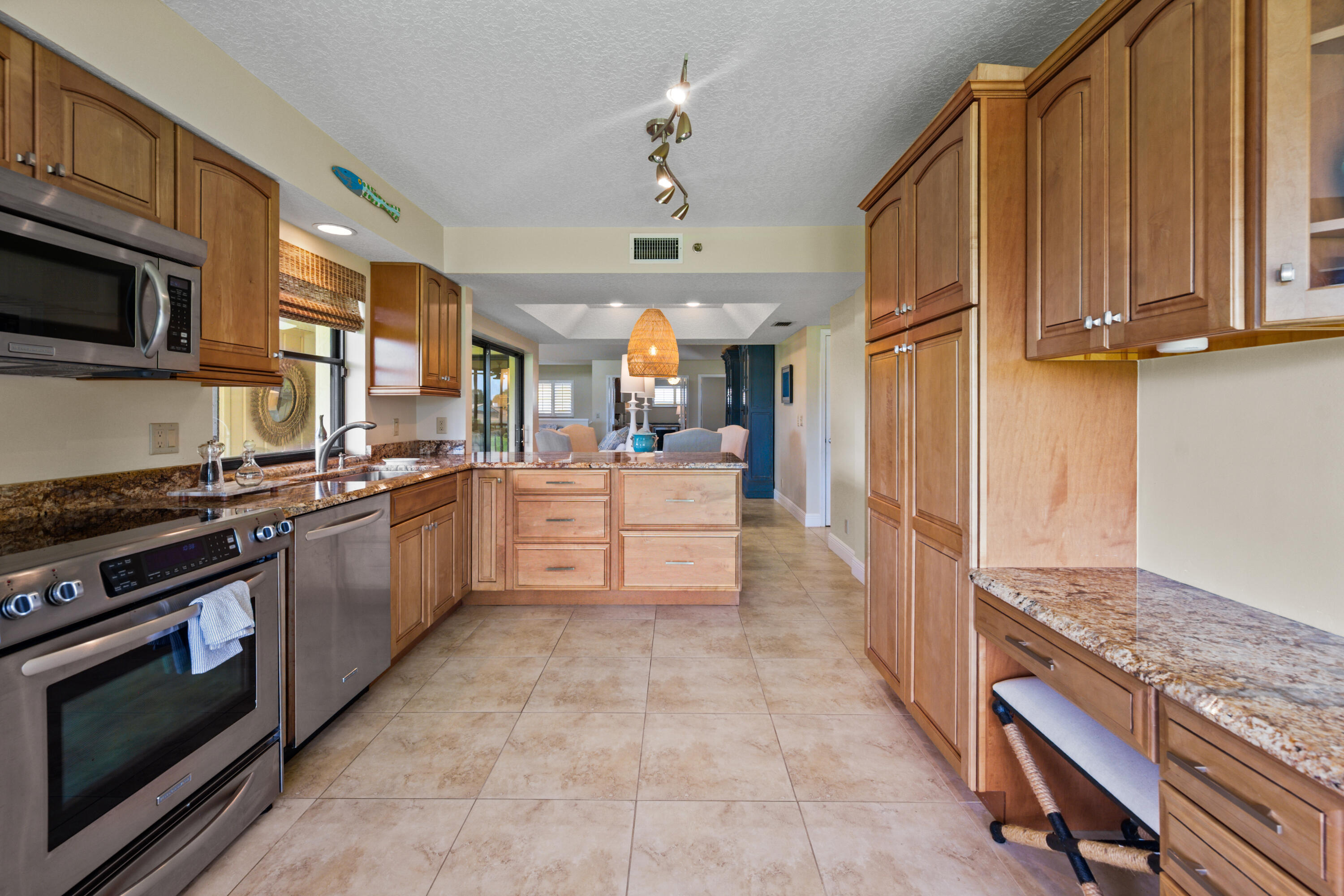 Kitchen with warm wood cabinets, granite counters, stainless appliances, and a central island opening to the living area.