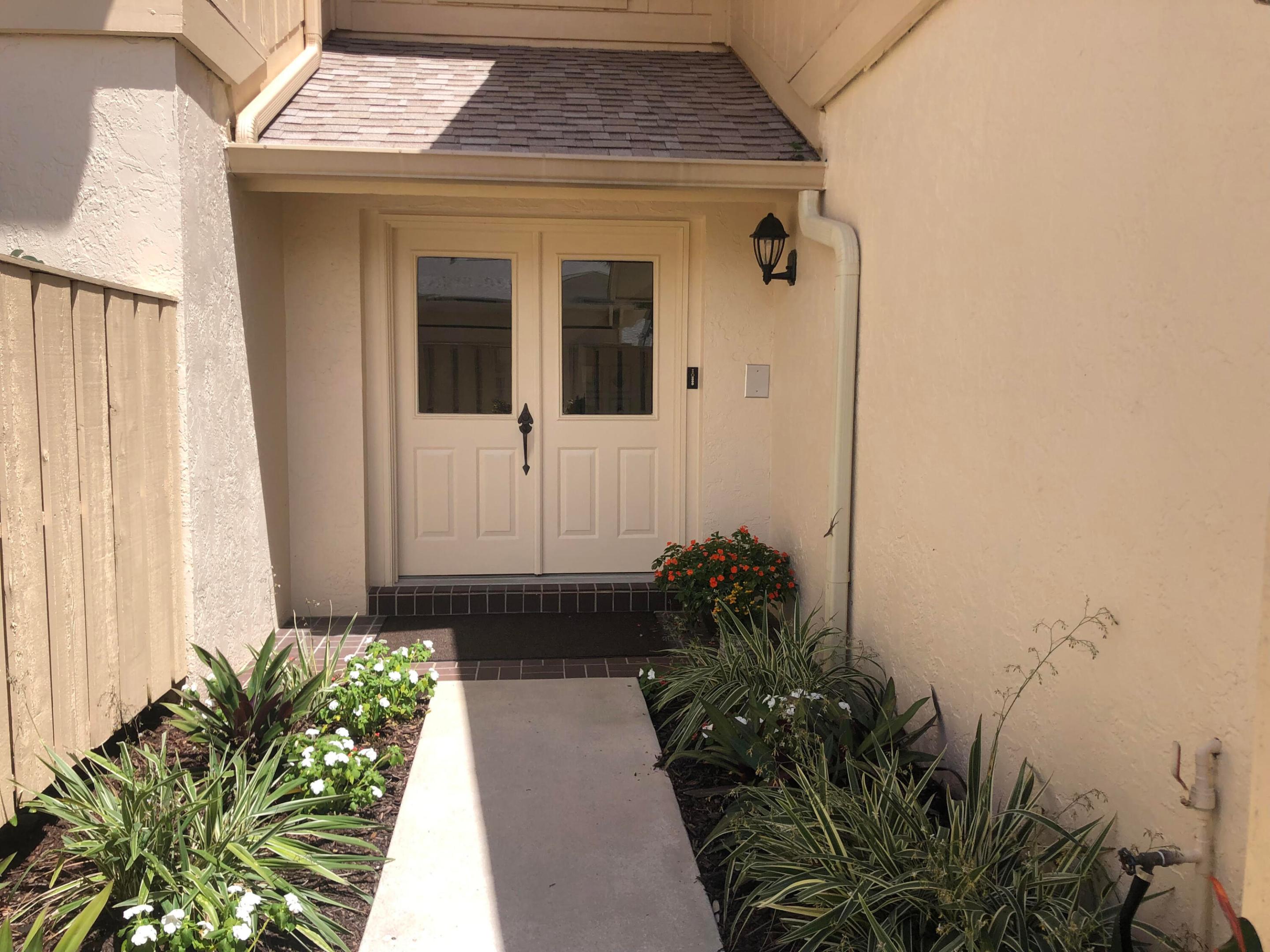 Covered home entrance with cream double doors and a flower-lined walkway.
