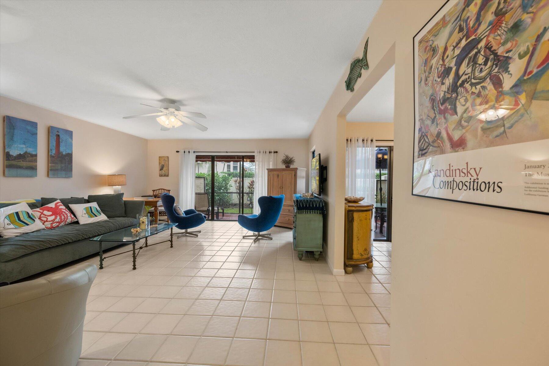 Furnished living room with blue lounge chairs, a gray sofa, and sliding glass doors to a garden.