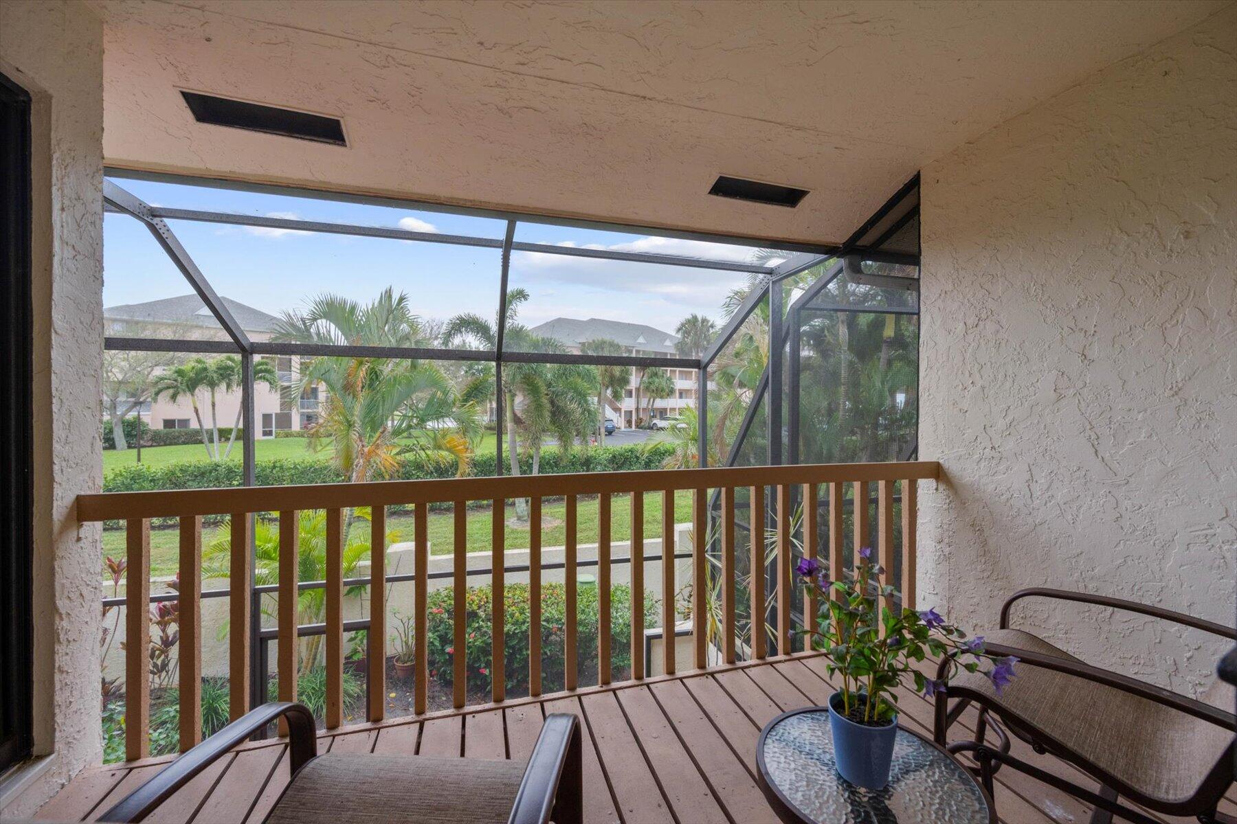 Screened balcony with wood decking, patio furniture, and views of palm trees and landscaped grounds.