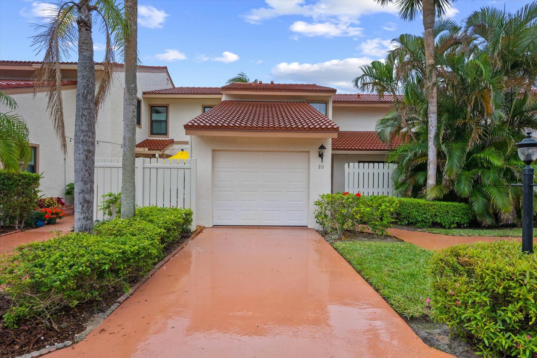 Townhouse exterior with a red tile roof, garage, tropical landscaping, and palm trees.
