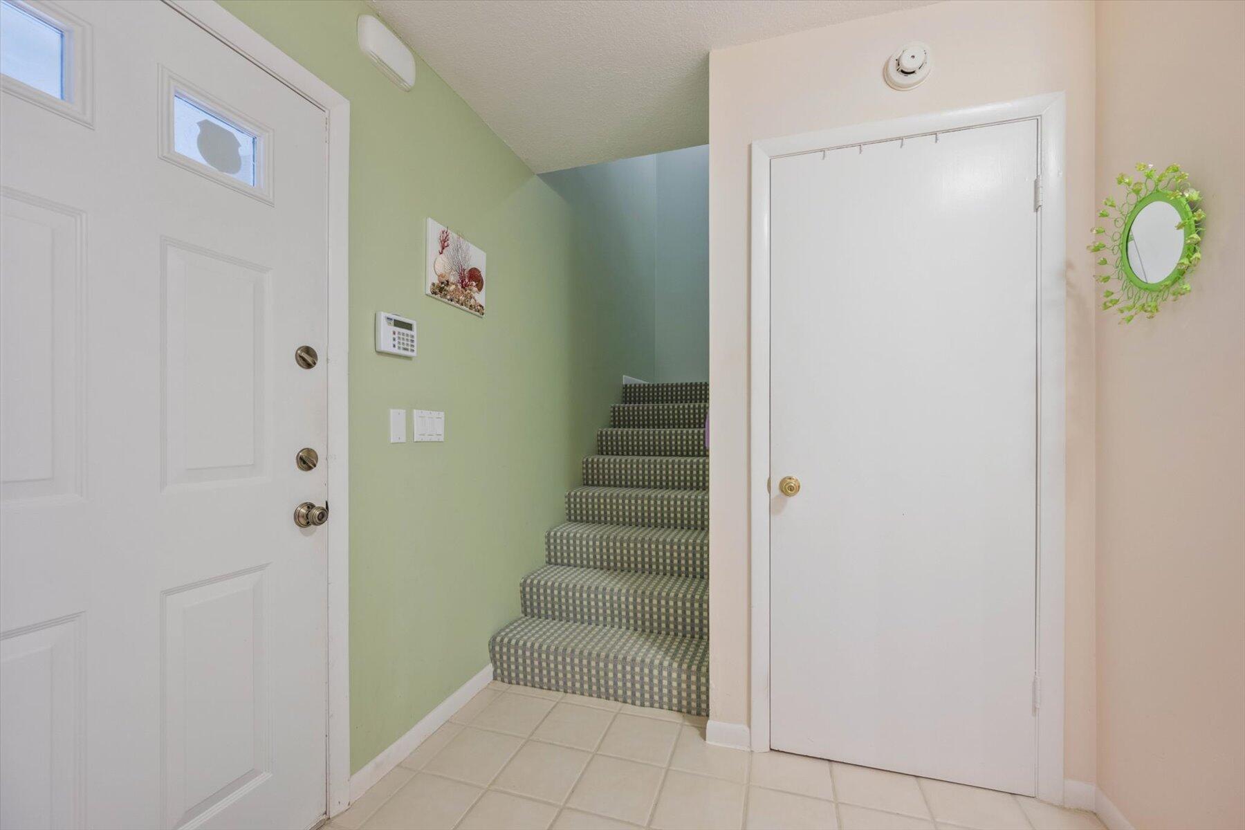 Entryway with tiled floor and carpeted stairs between pale green walls.
