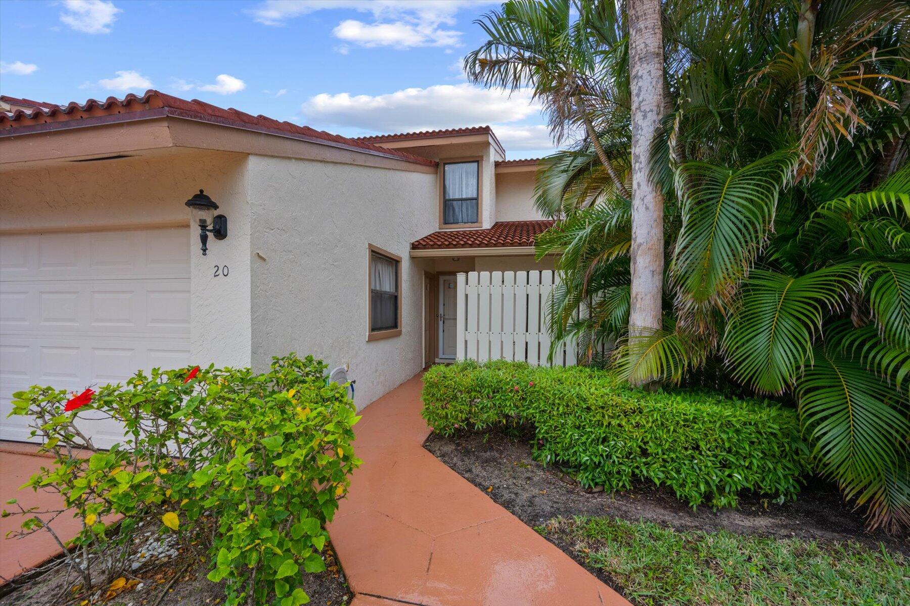Two-story home exterior with a terracotta tile roof, white garage, and palm-lined entry.