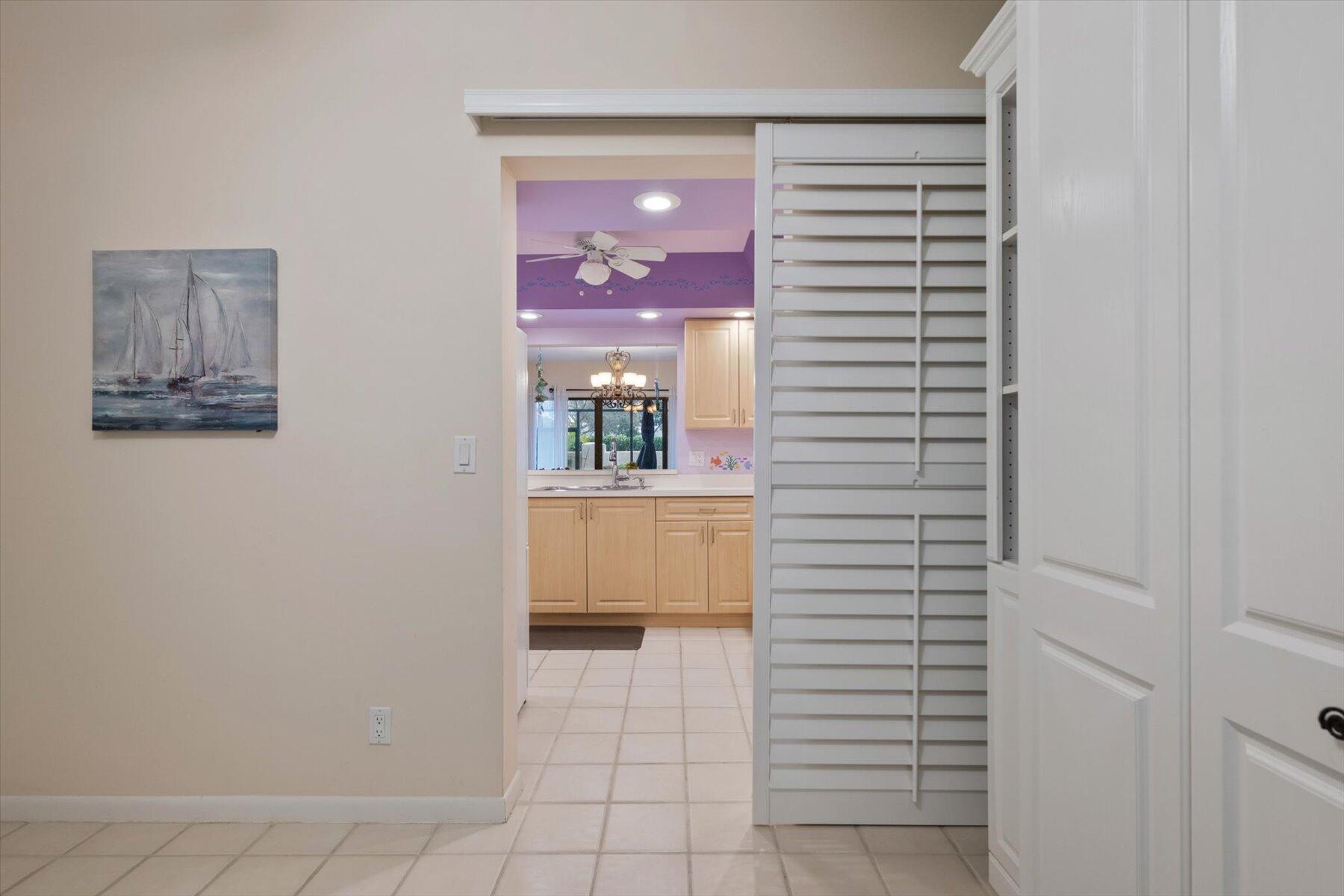 Tiled hallway looking into a kitchen, with light wood cabinets and an open louvered closet.