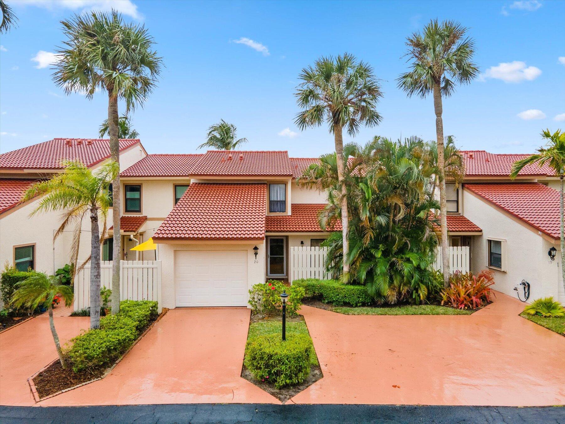 Townhouse with a red tile roof, garage, white fencing, and tall palms in front.