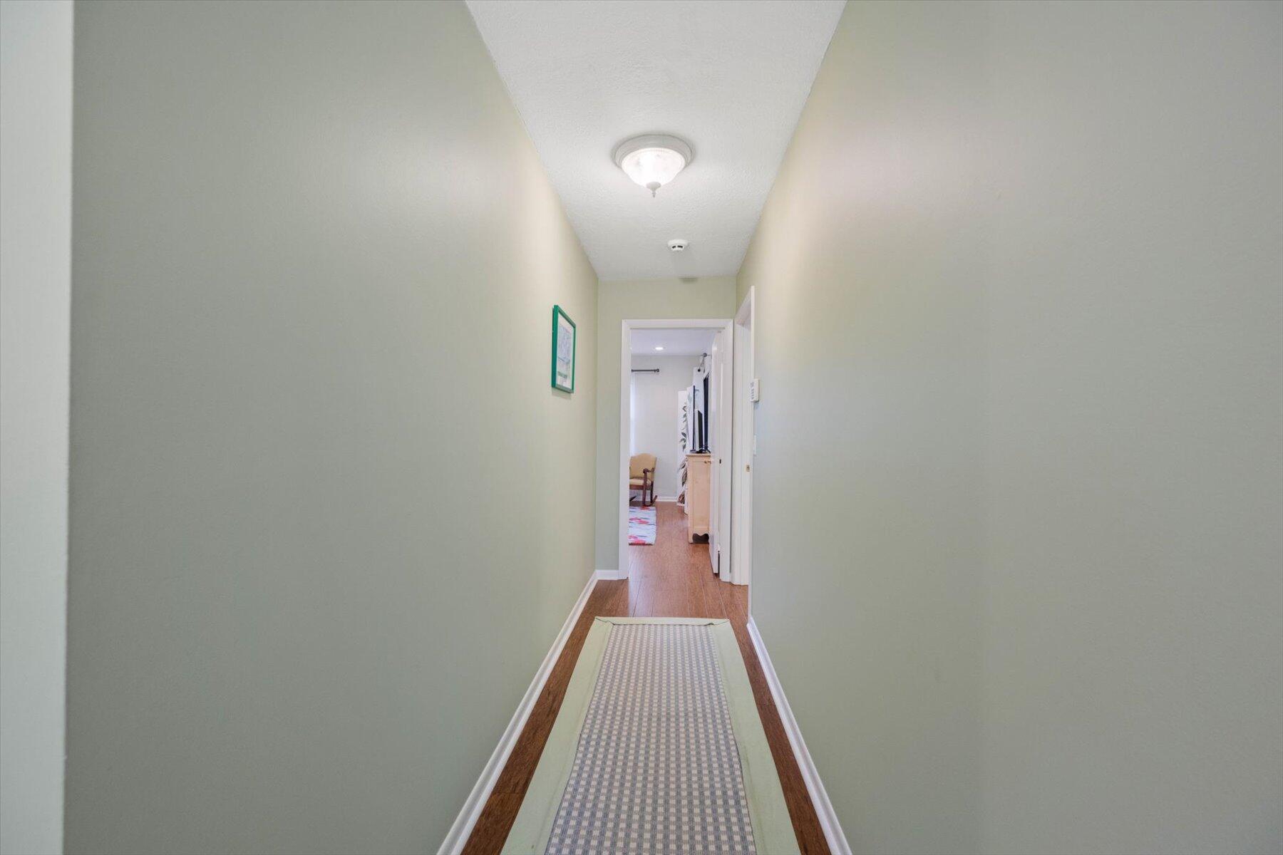 Hallway with pale green walls, hardwood floors, and a patterned runner leading to an open doorway.