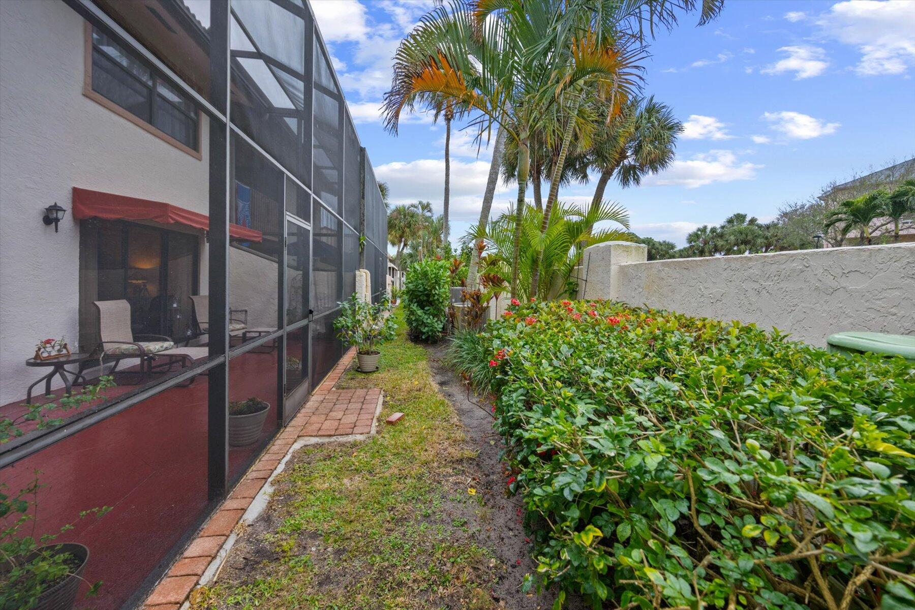 Screened patio beside a tropical garden with palms, flowering shrubs, and a brick walkway.