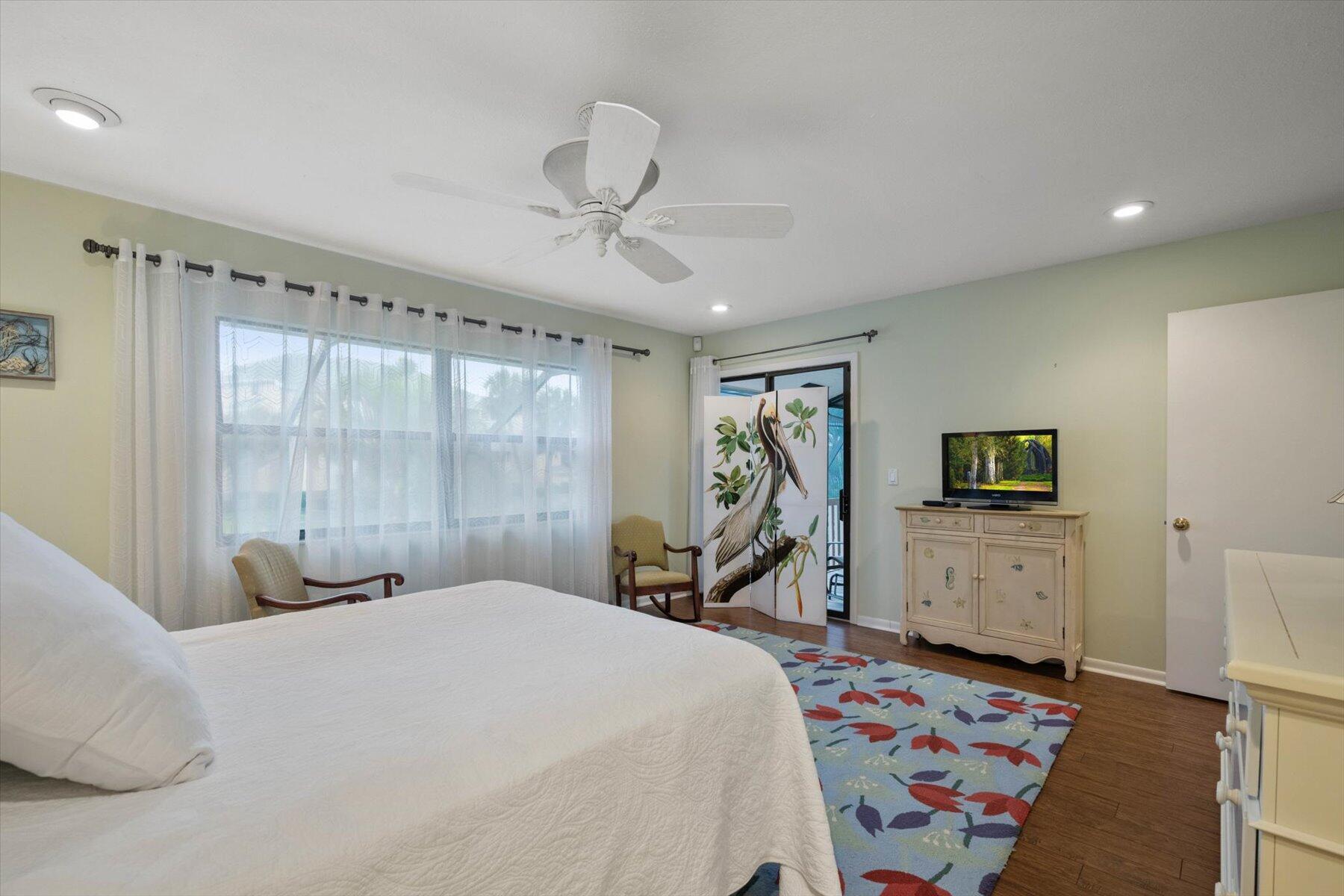 Bedroom with a large white bed, sheer-curtained windows, and a colorful floral rug.