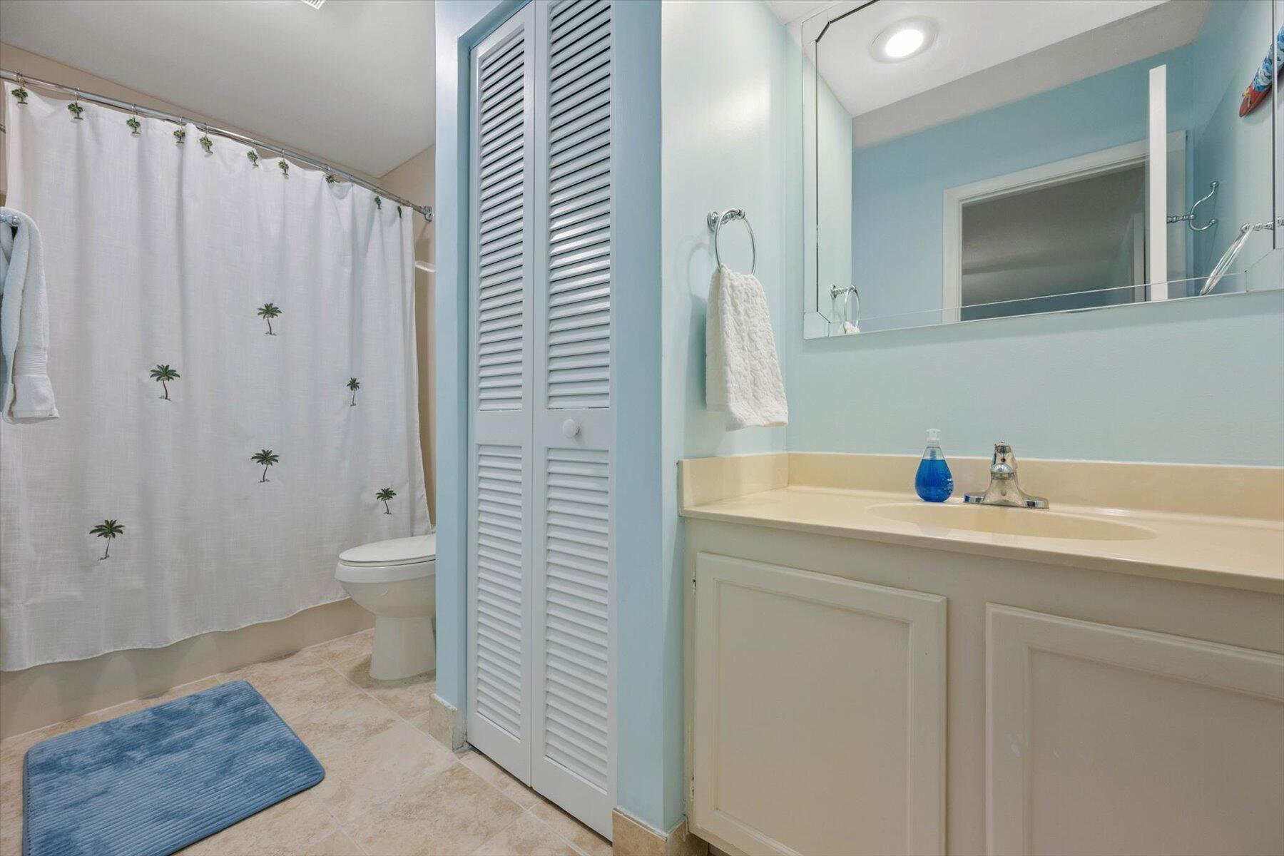 Bathroom with a cream vanity, pale blue walls, and a palm-print shower curtain.
