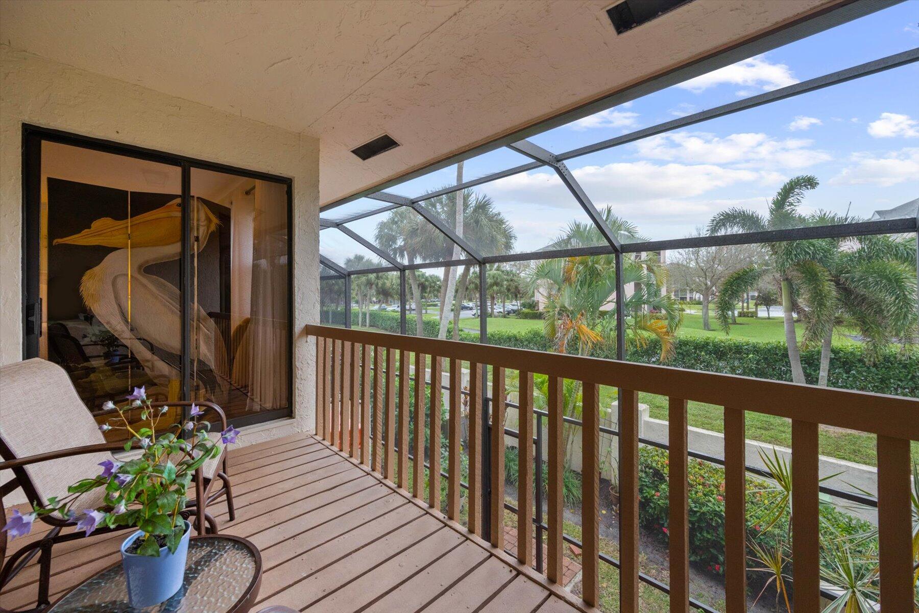 Apartment balcony with screened enclosure and wooden railing overlooking palm-lined landscaped grounds.