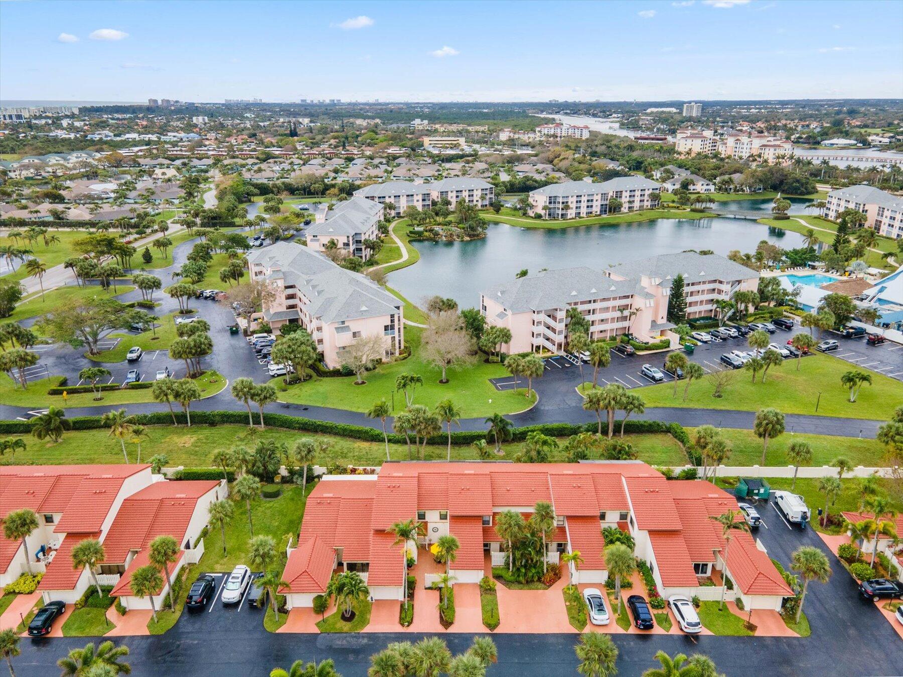 Aerial view of a Jupiter condominium community around a lake, with a pool and red-roofed townhomes.