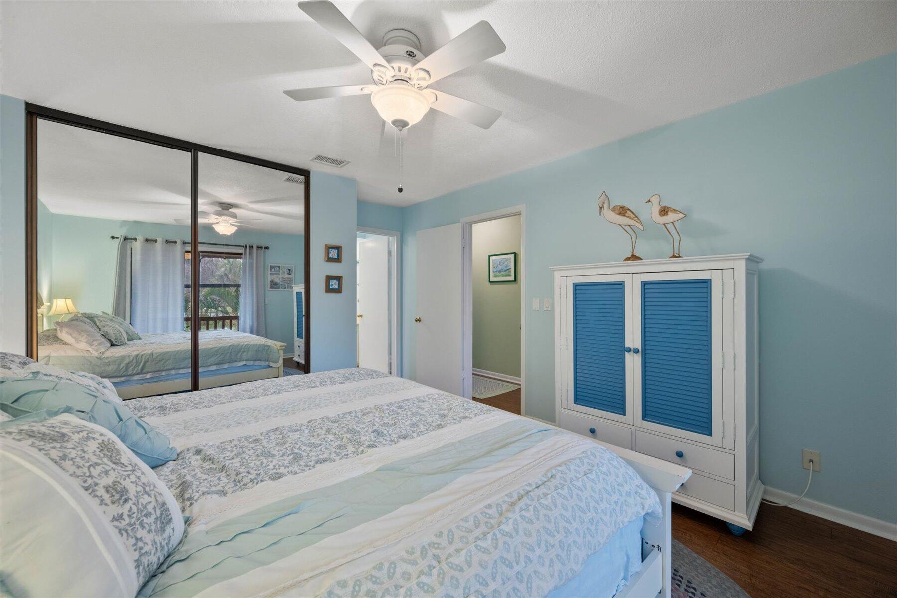 Bedroom with pale patterned bedding, mirrored closet doors, and a white cabinet with blue louvered doors.