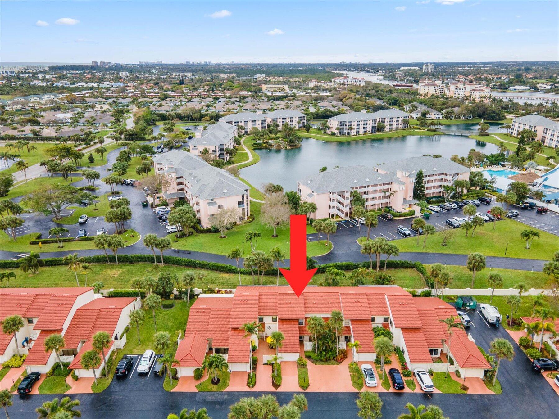 Aerial view of a Jupiter townhome community; a red arrow marks a terracotta-roofed unit beside a lake.