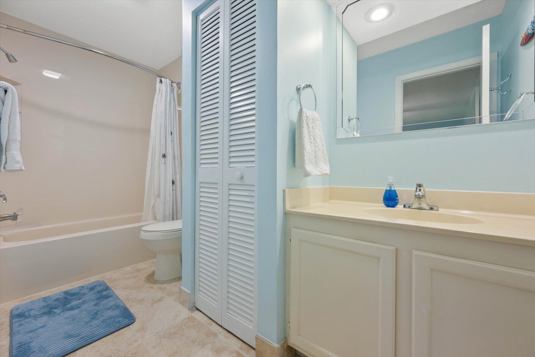 Bathroom with a tub and shower, toilet, and cream vanity against pale blue walls.