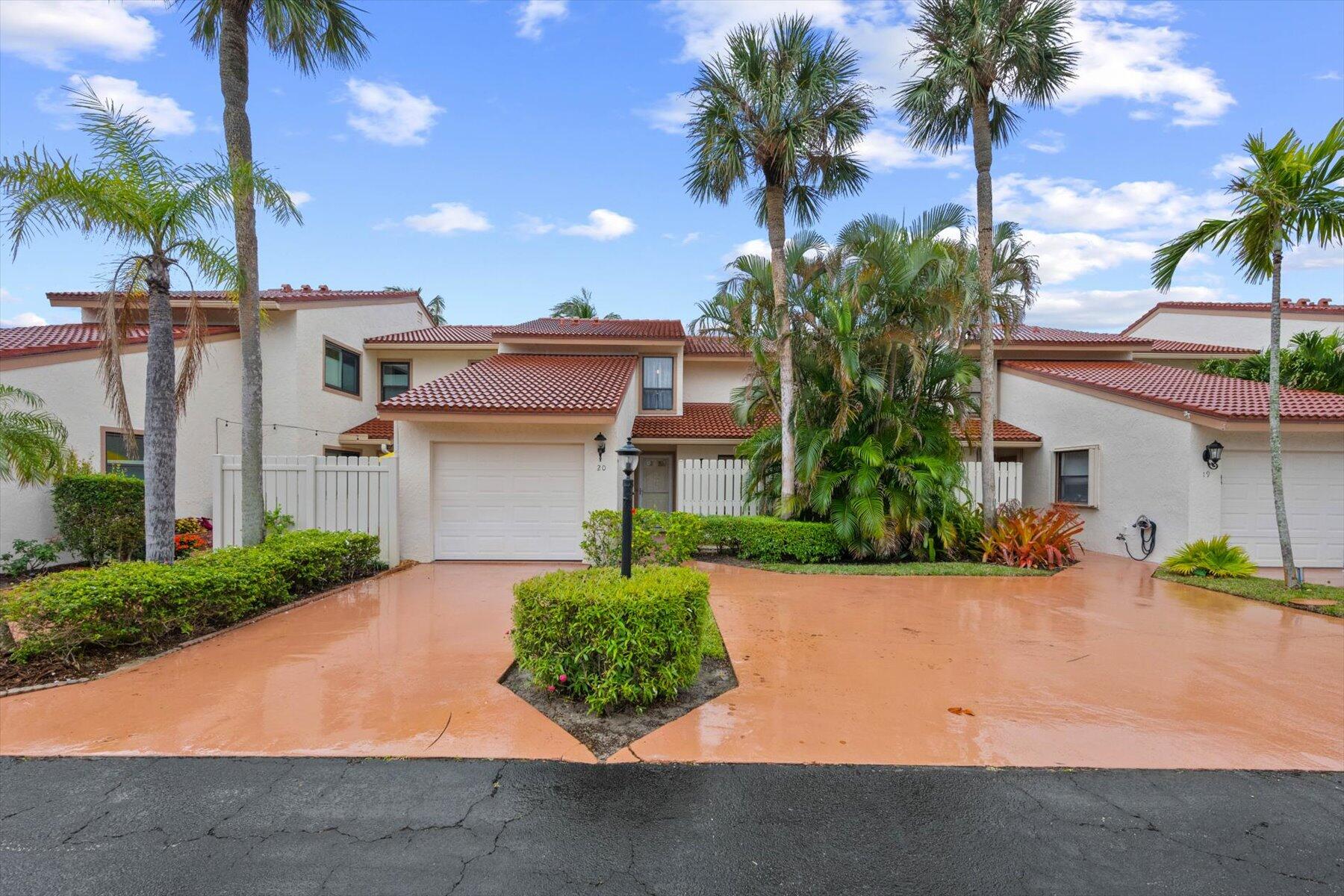 Two-story stucco townhouse with red tile roofs, attached garage, palms, and a broad driveway.