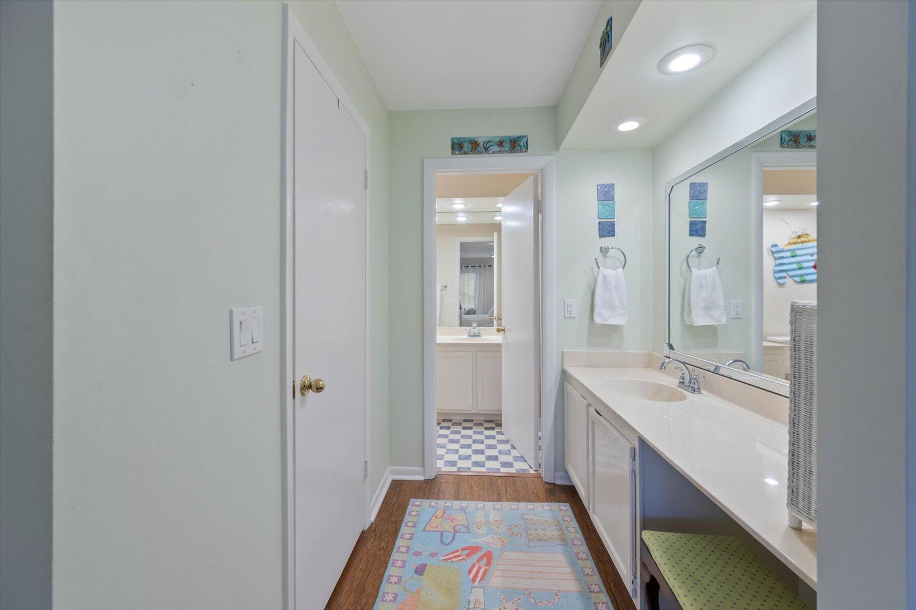 Bathroom with a long white vanity and mirror, opening onto a second vanity area with checkerboard flooring.
