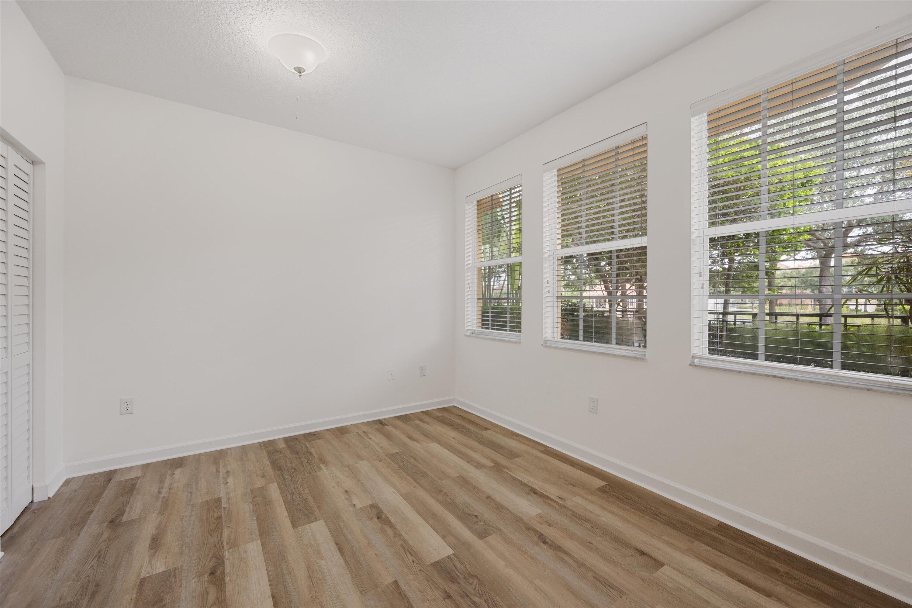 Empty room with wood-look flooring, a louvered closet door, and three windows with blinds.