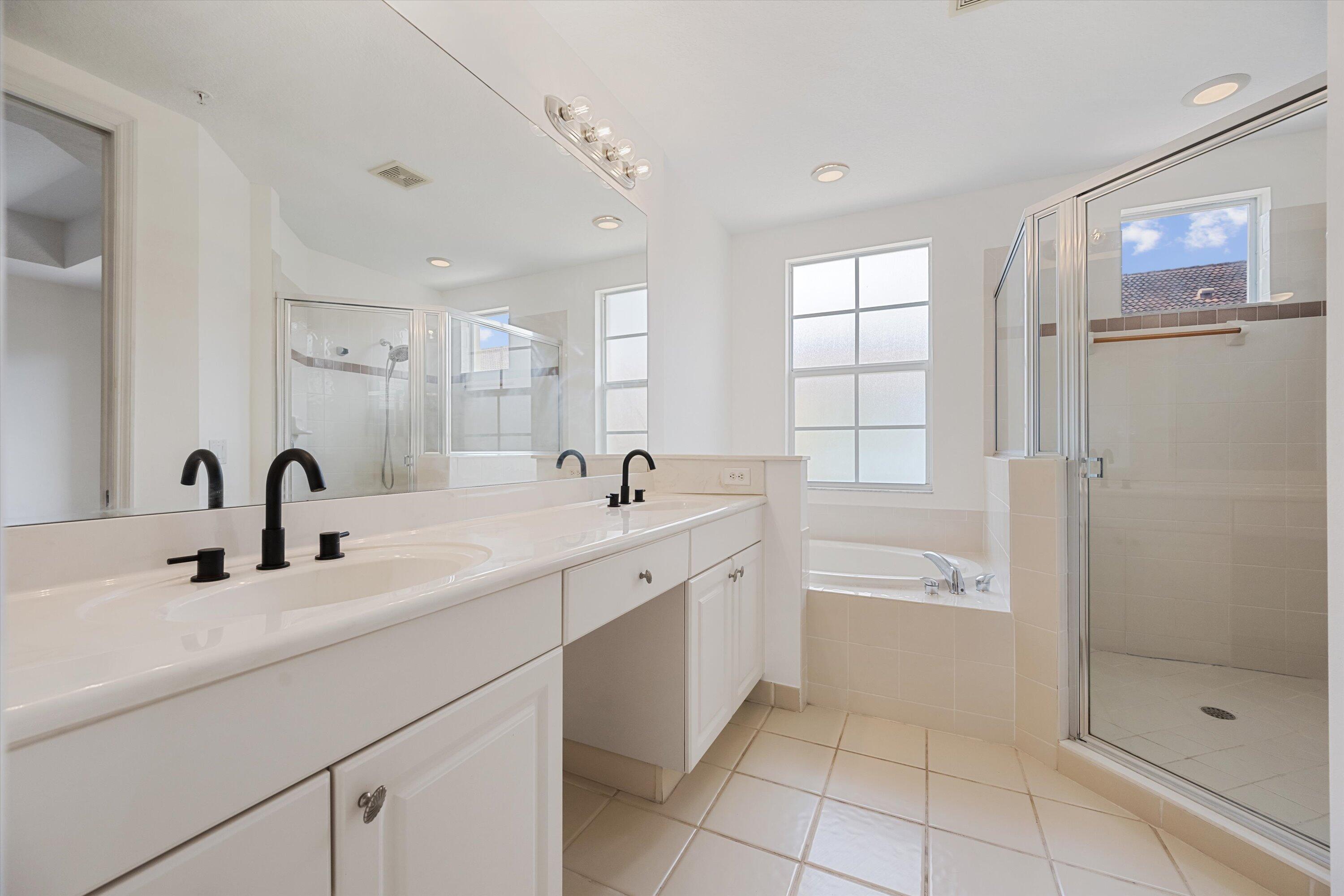 Bright bathroom with a double-sink vanity, tiled tub, and glass-enclosed shower.