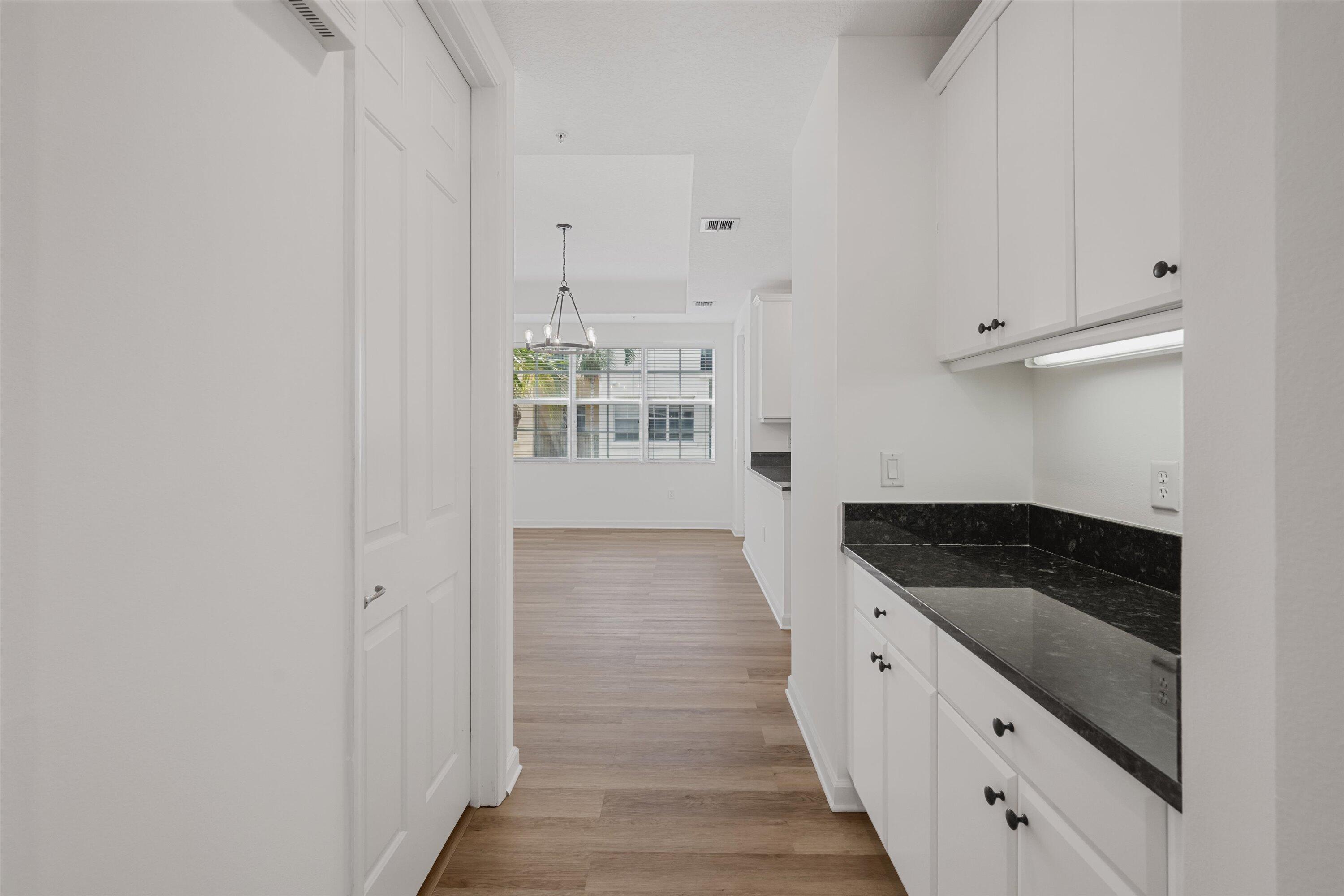 Kitchen with white cabinets and dark countertops opening onto a dining area with a large window.
