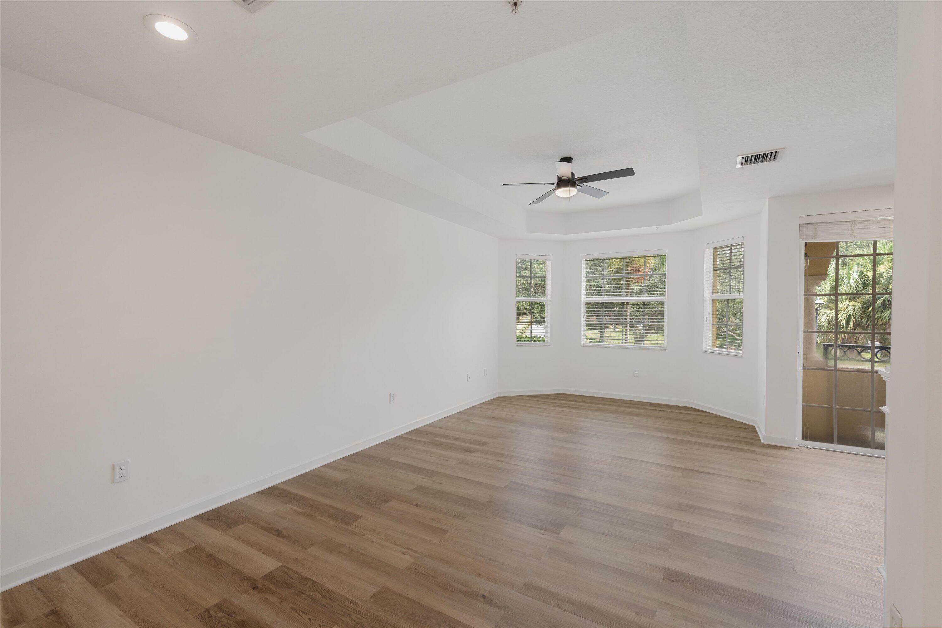 Empty room with wood-look floors, a tray ceiling, several windows, and a glass door to the patio.