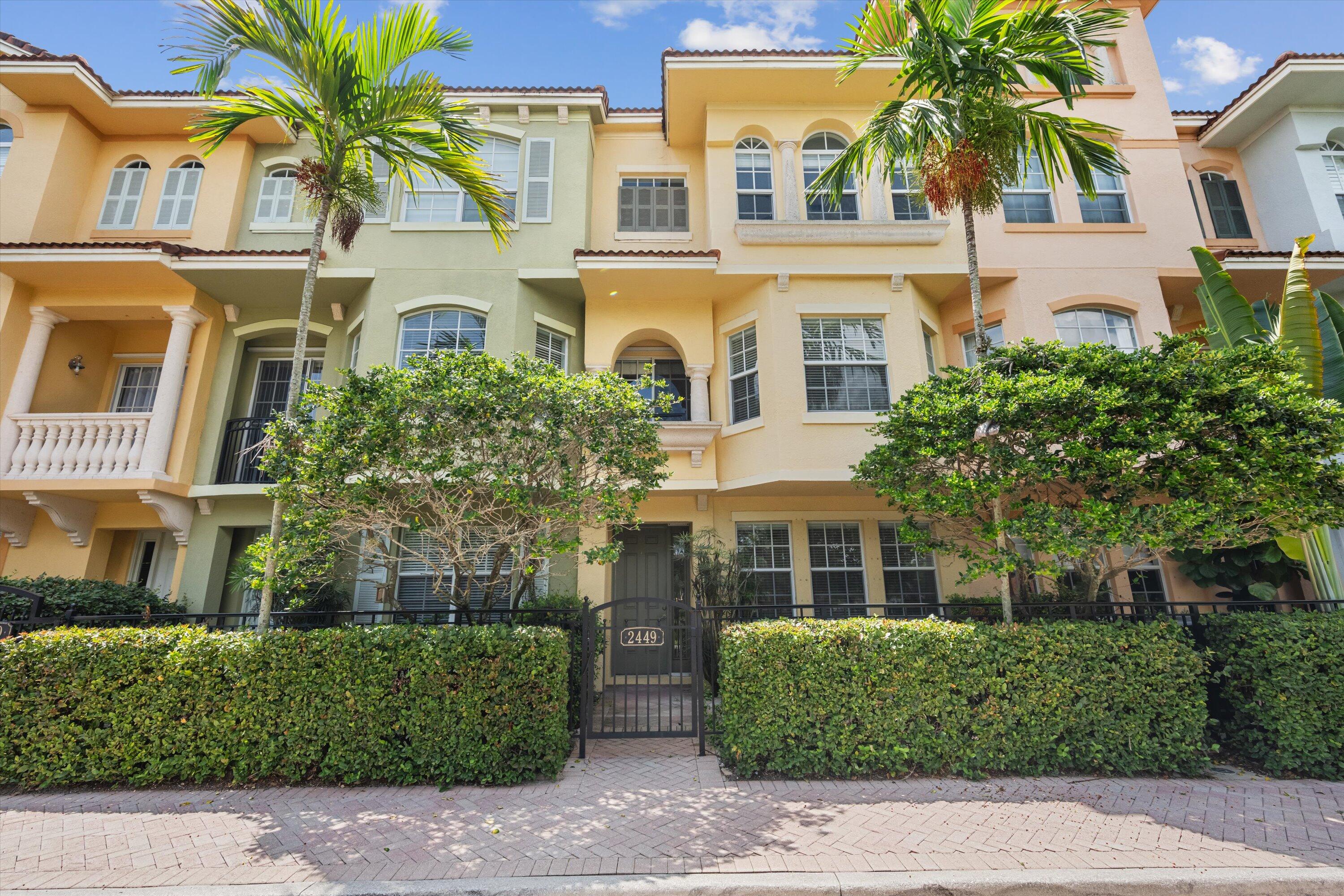 Attached residence with pastel stucco facades, palm trees, and hedge-lined entrance gate marked 2449.