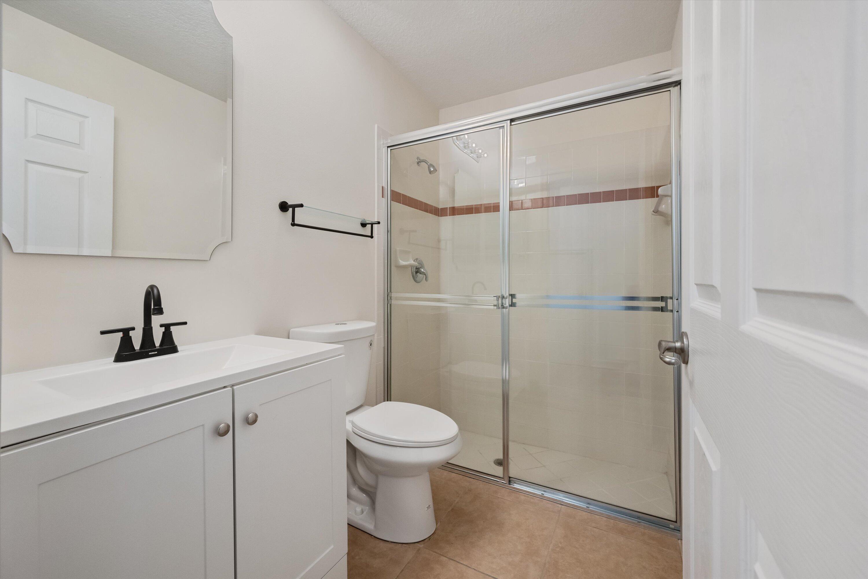 Bathroom with a glass-enclosed shower, tiled accent stripe, white vanity, and black faucet.