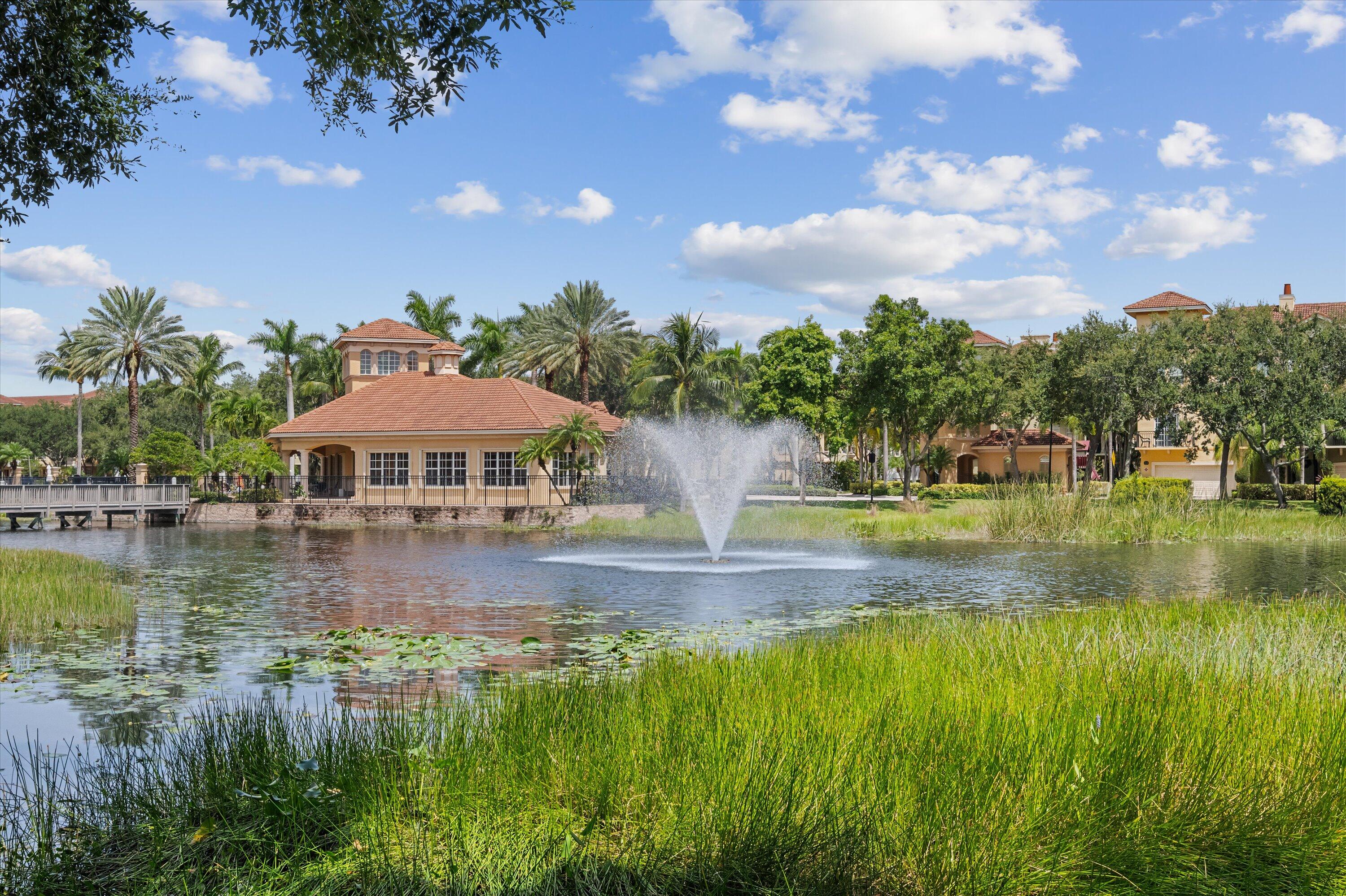Community pond with fountain, palms, and tile-roofed homes along the shore.