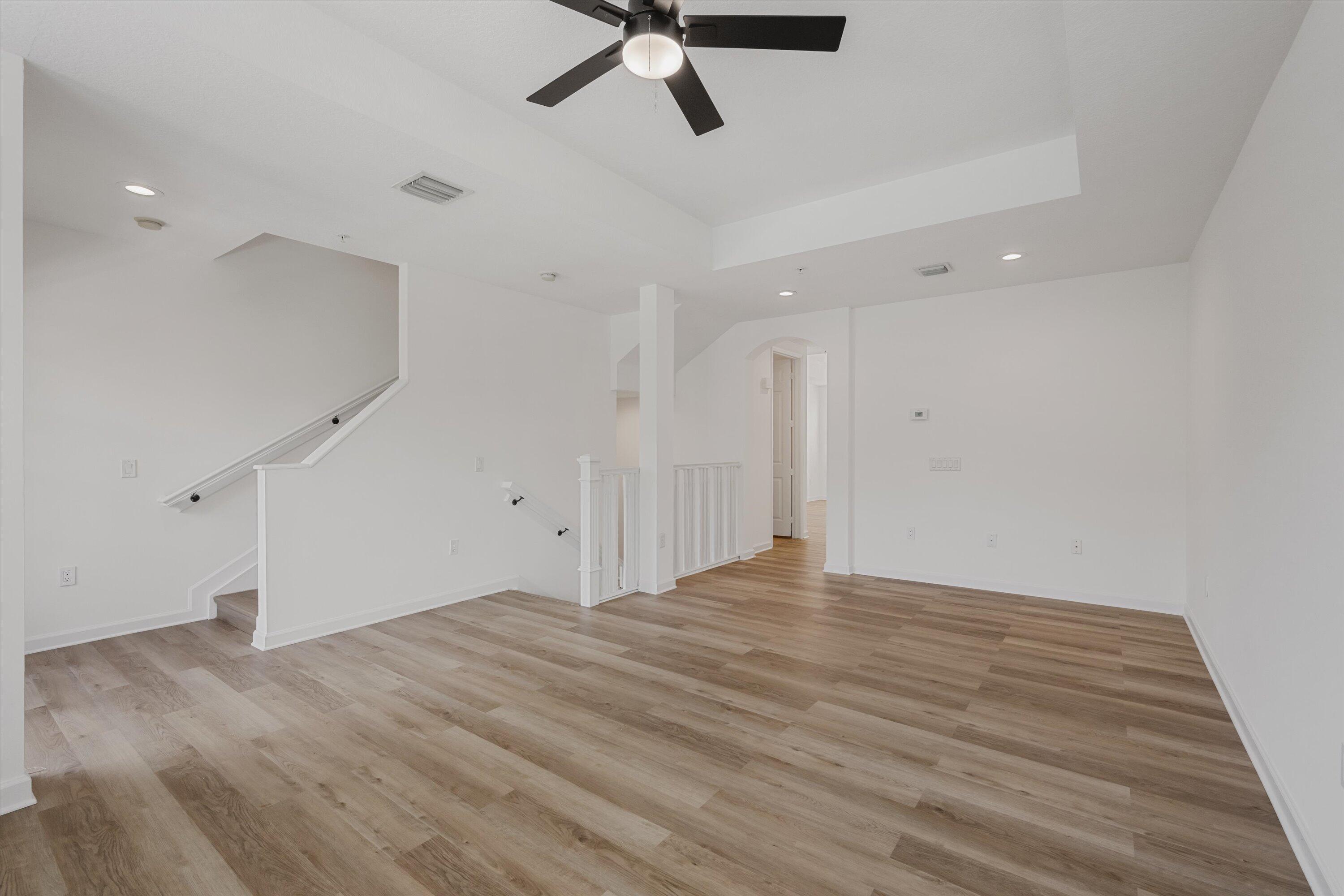 Vacant interior room with light wood floors, a black ceiling fan, and a staircase railing.