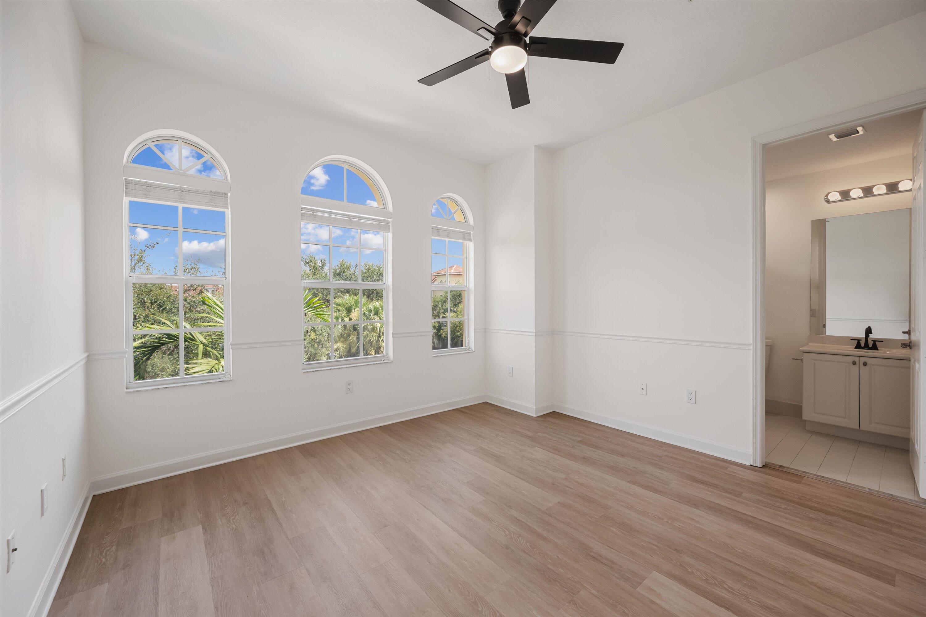 Unfurnished bedroom with three arched windows, wood-look flooring, and an ensuite bathroom doorway.
