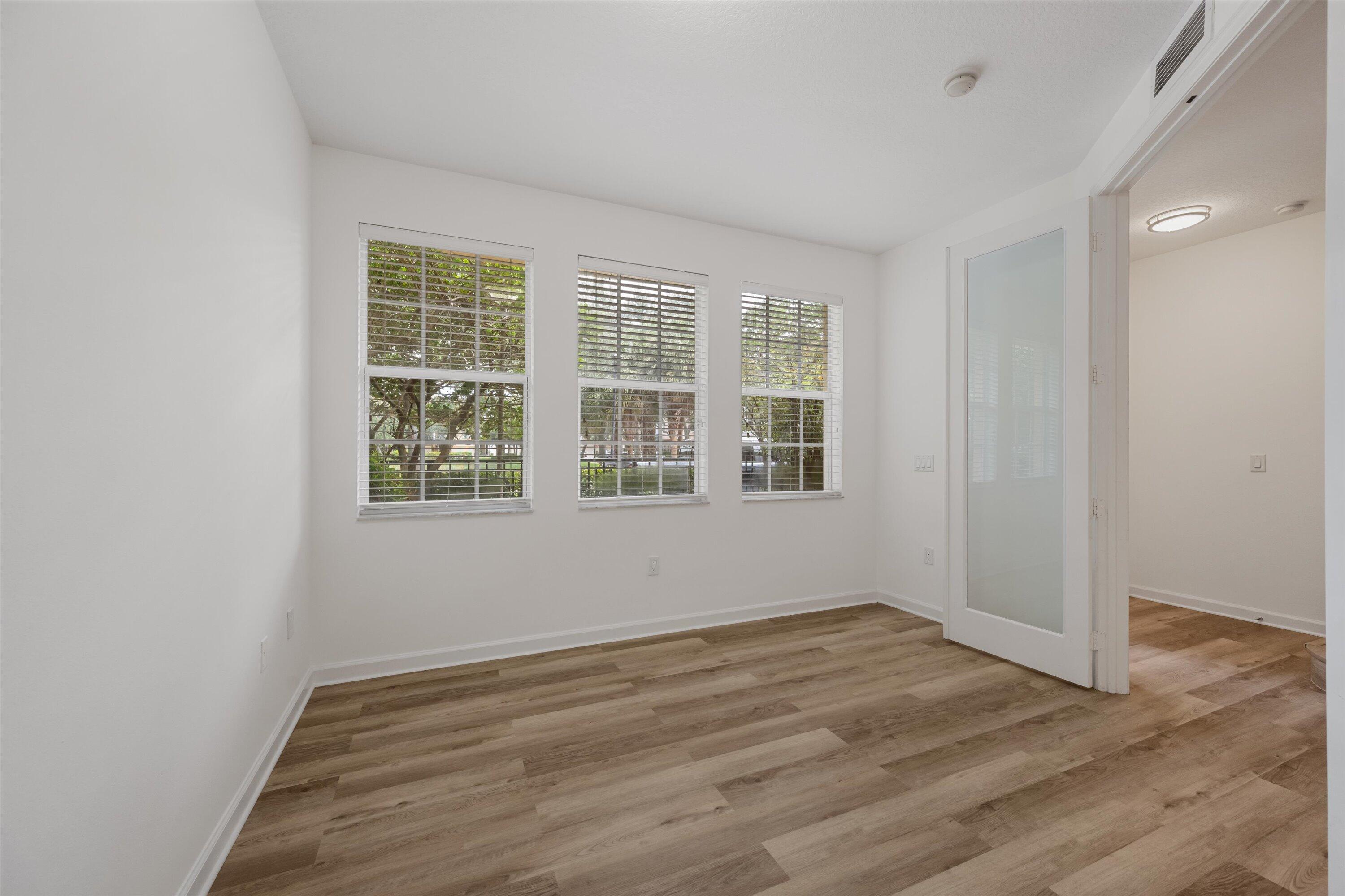 Empty room with wood-look flooring, three window blinds, and an open glass-panel door.