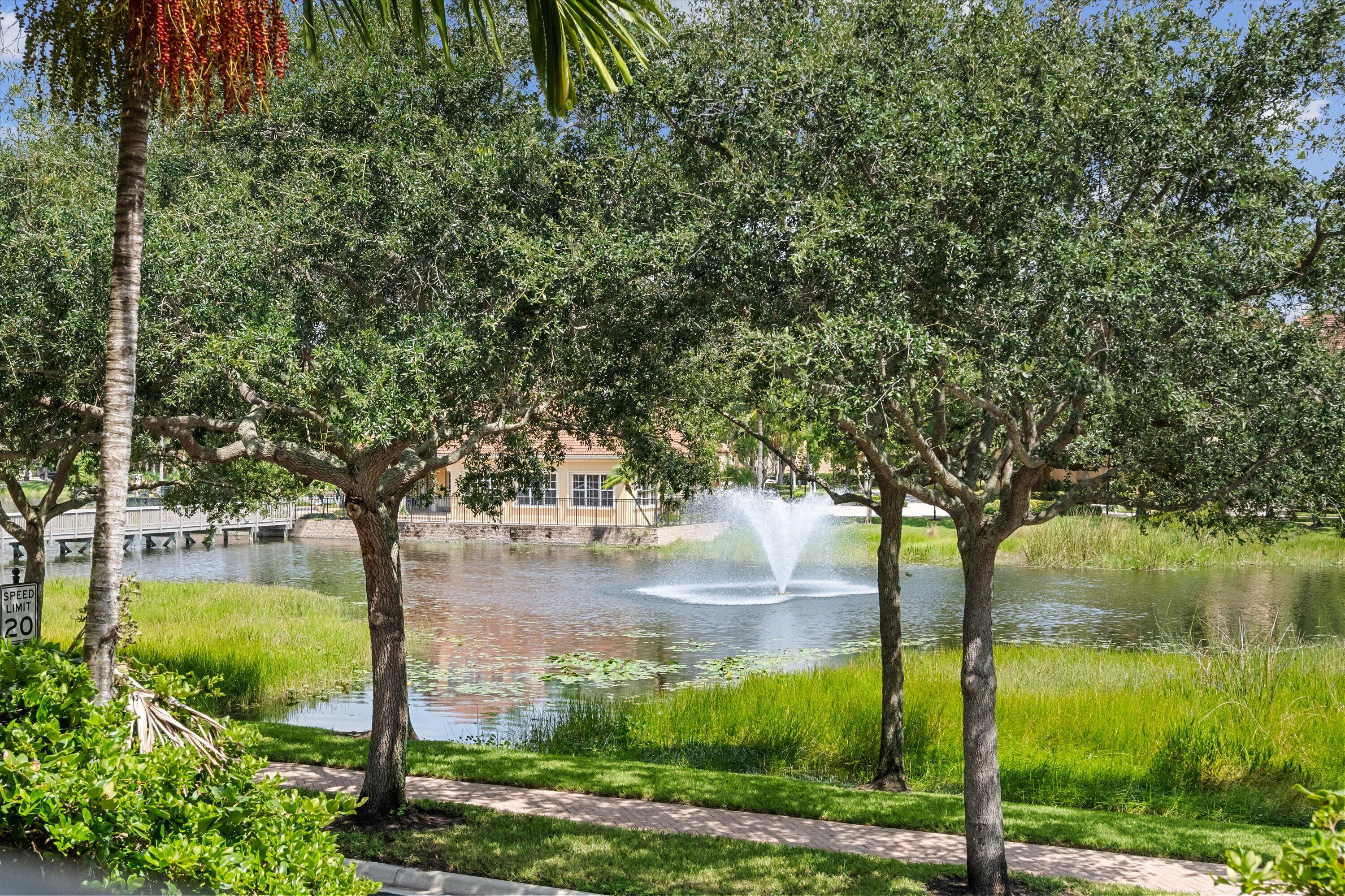 Community pond with a fountain, framed by mature trees and a waterside walkway.