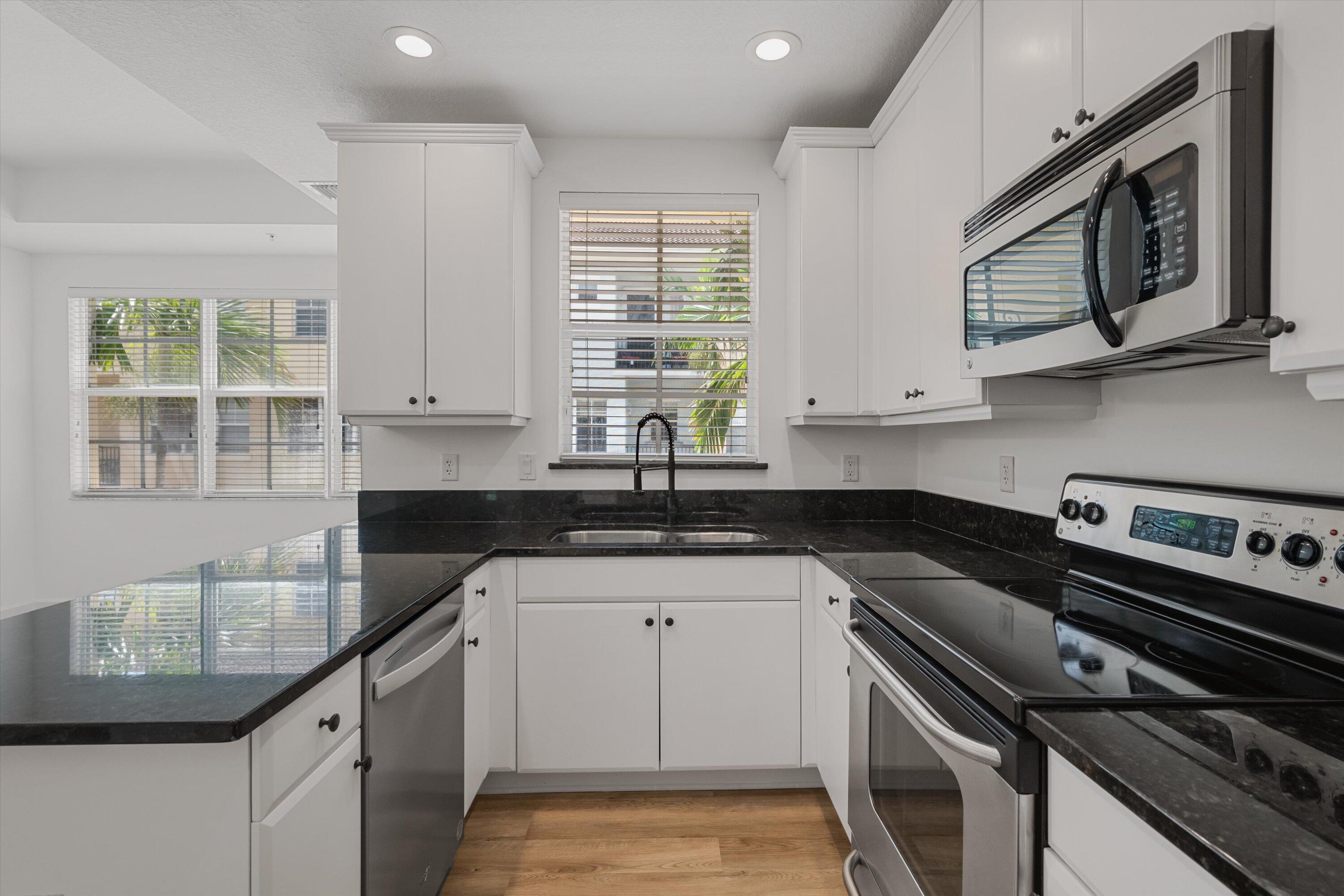 Kitchen with white cabinets, black granite counters, stainless appliances, and a double sink beneath a window.