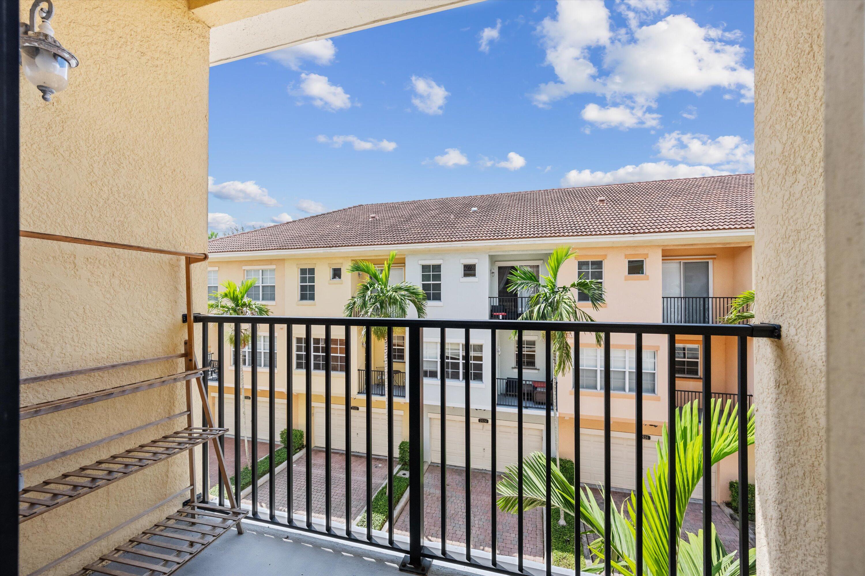 Apartment balcony overlooking palm trees, a paved courtyard, and neighboring residences.