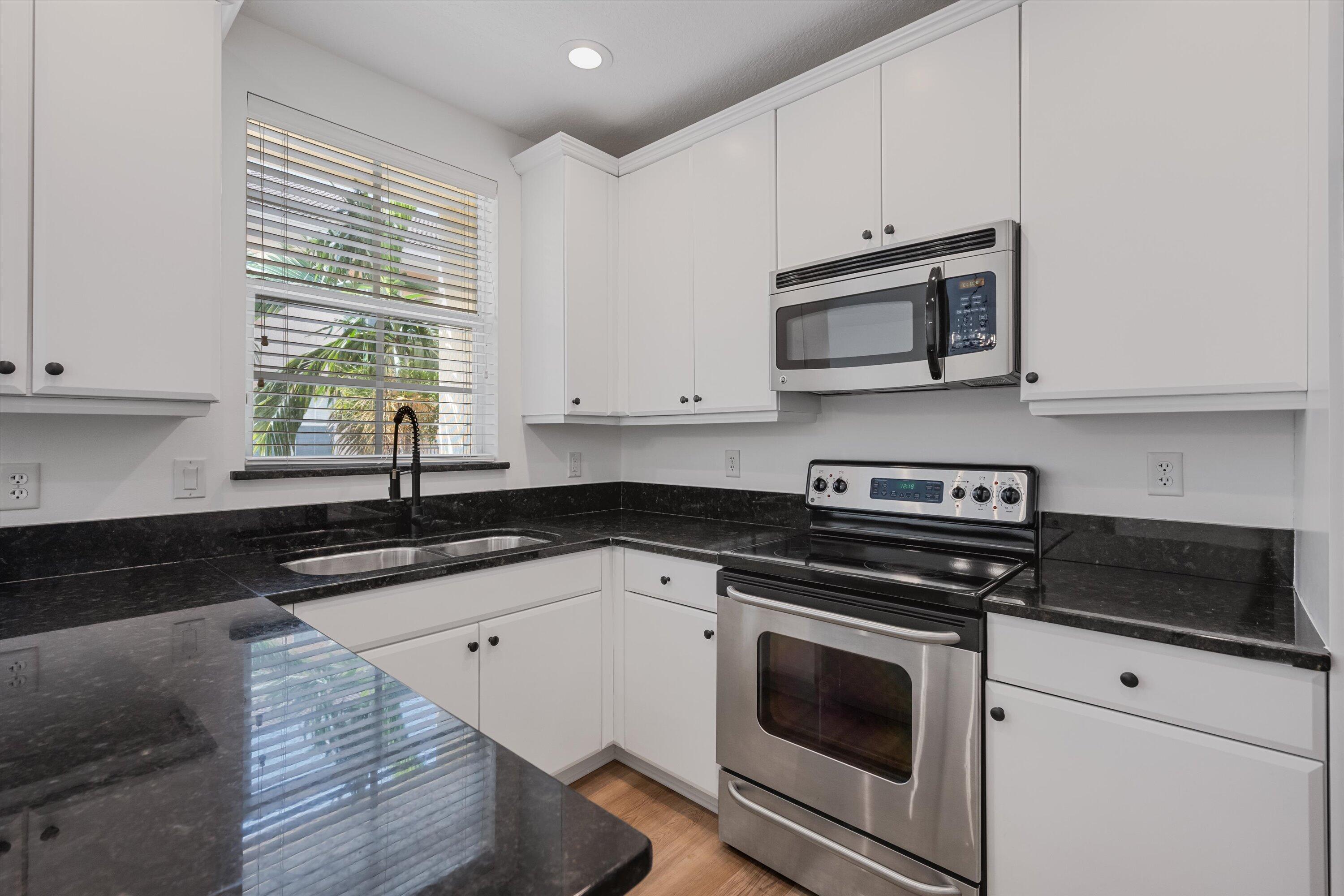 Kitchen with white cabinets, black stone counters, stainless appliances, and a window above the sink.
