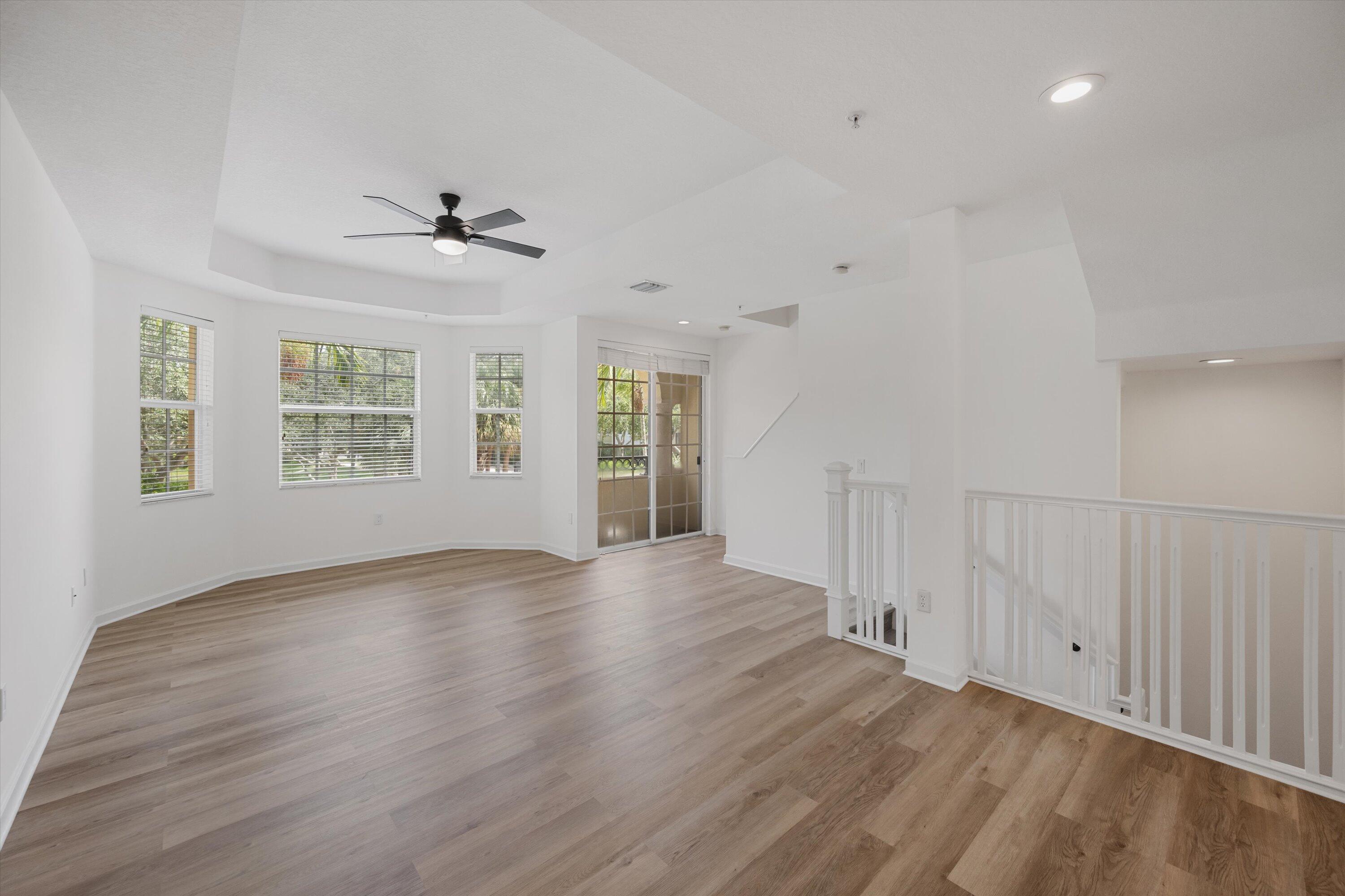 Vacant living area with light wood-look floors, shuttered windows, and sliding glass doors.