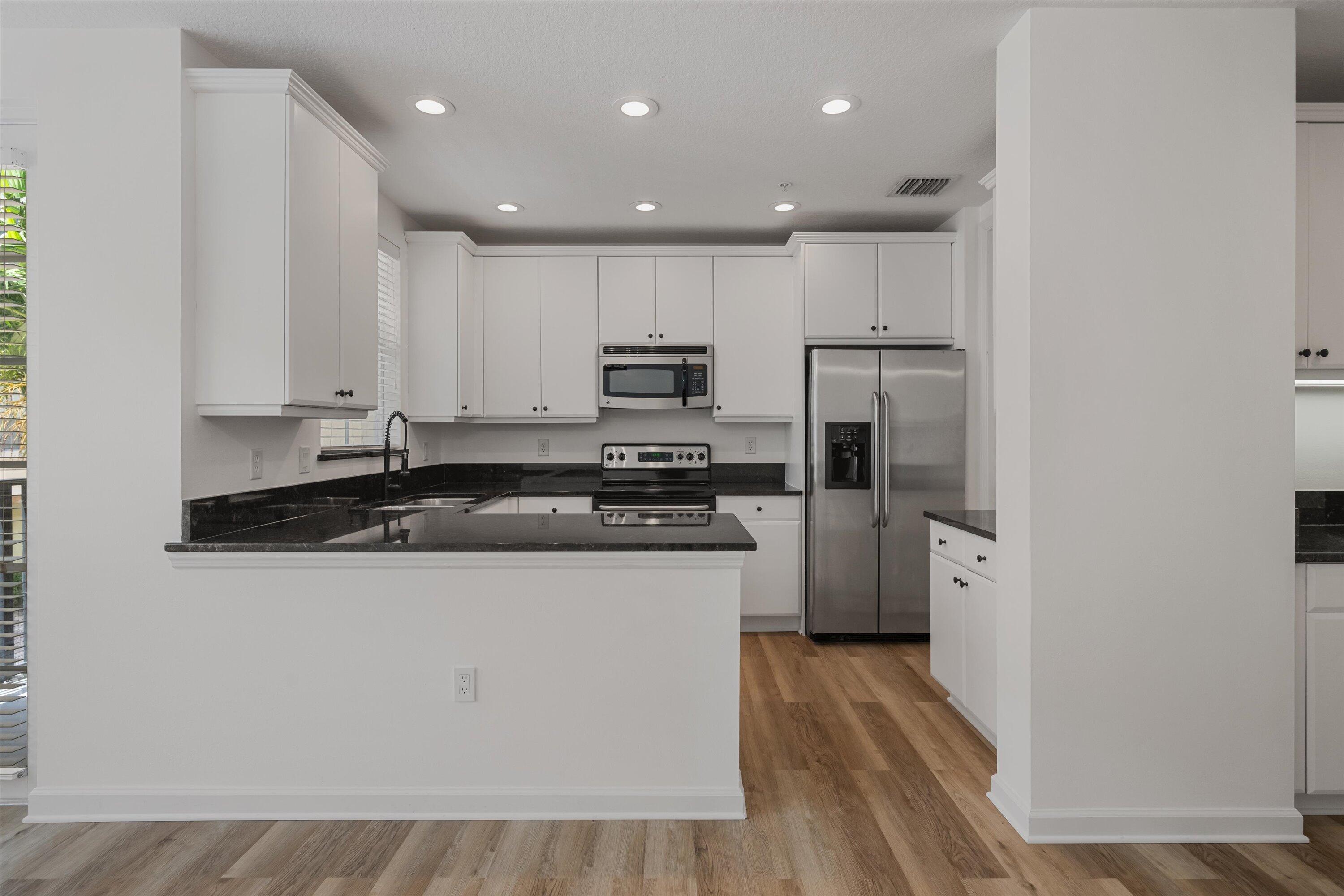 Kitchen with white cabinetry, black countertops, stainless steel appliances, and wood-look flooring.