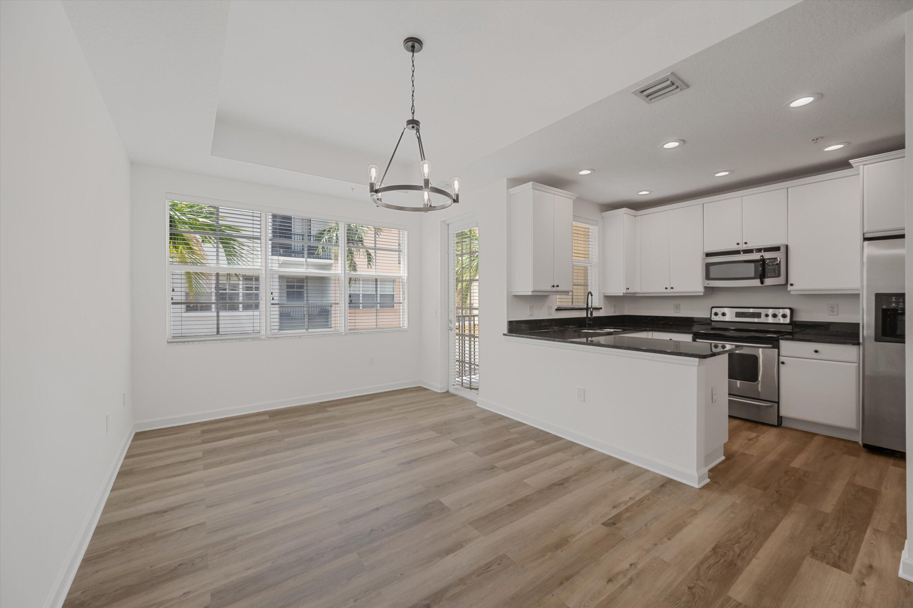 Open kitchen and dining area with white cabinets, stainless appliances, and large windows overlooking palm trees.