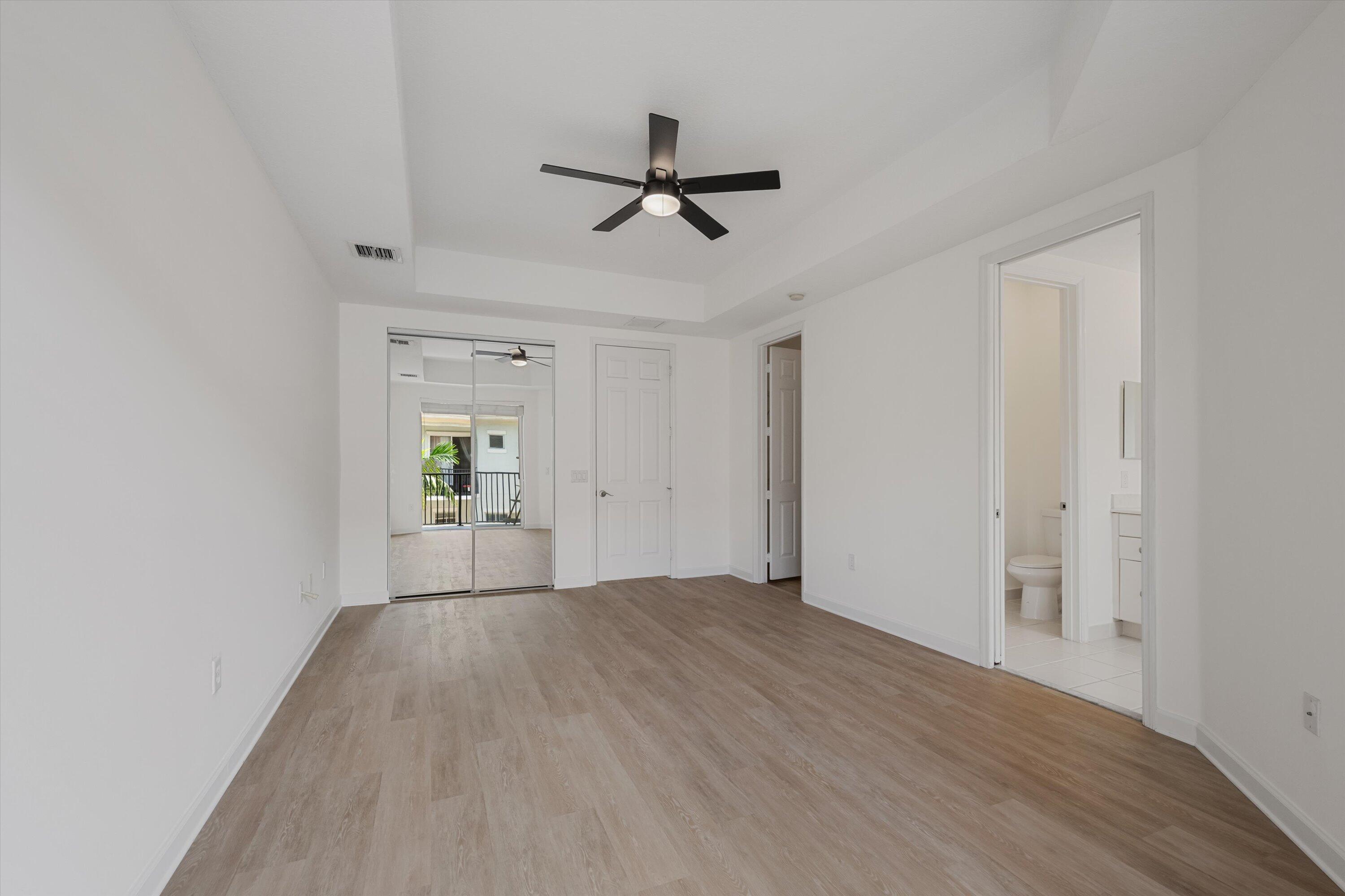 Empty bedroom with mirrored closet doors, a ceiling fan, and an ensuite bathroom doorway.
