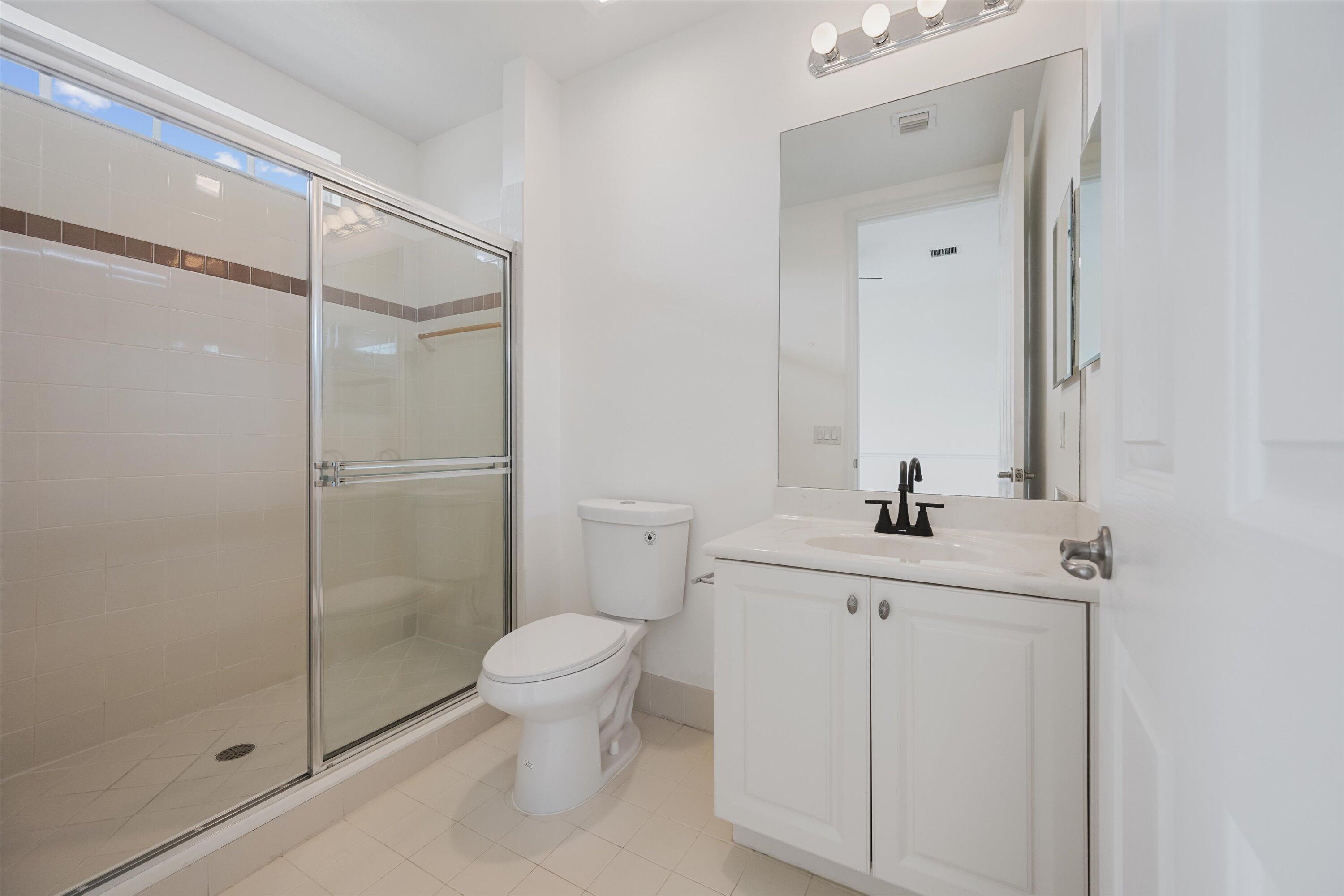 Bathroom with a glass-enclosed tiled shower and white vanity beneath a large mirror.