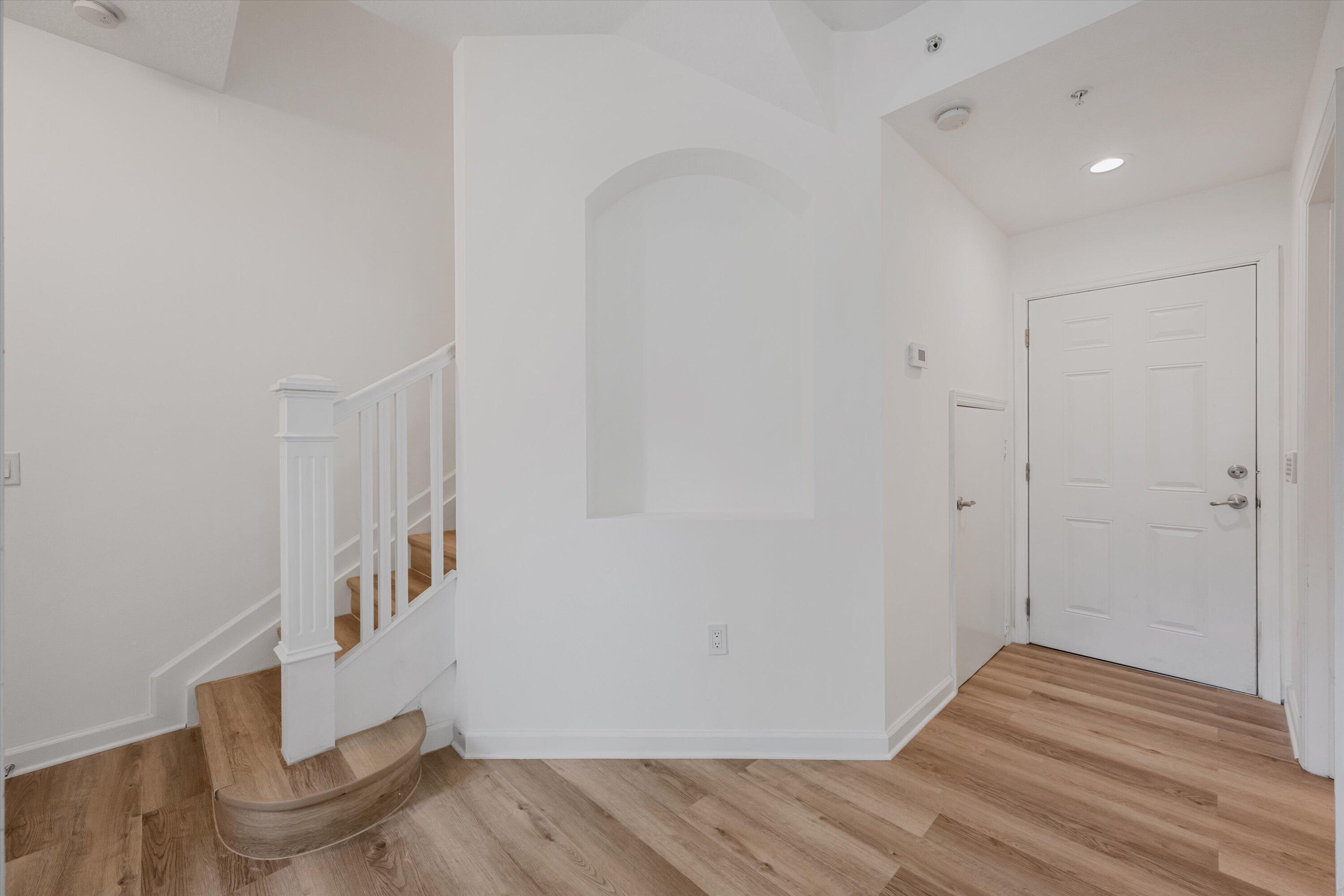 Entry foyer with a curved wooden staircase, white paneled front door, and light wood flooring.