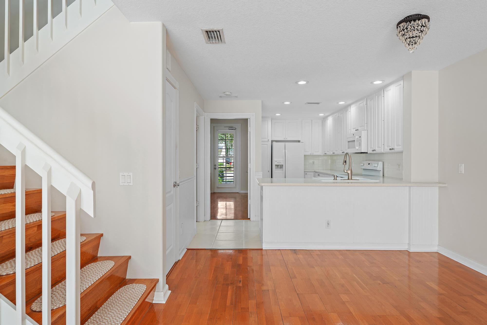 Open kitchen and dining area with white cabinetry, a breakfast bar, hardwood floors, and a wood staircase.