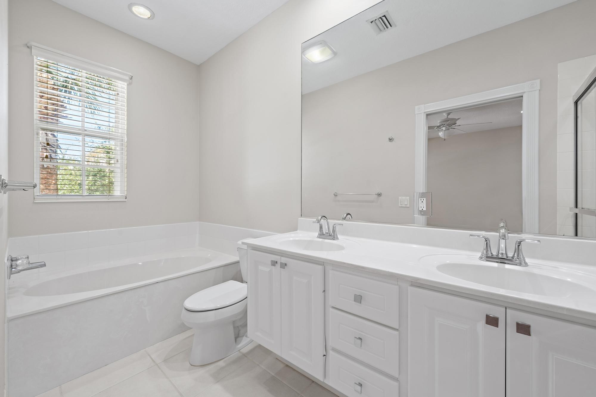 Bathroom with a white double-sink vanity, large mirror, and built-in bathtub beside a window.