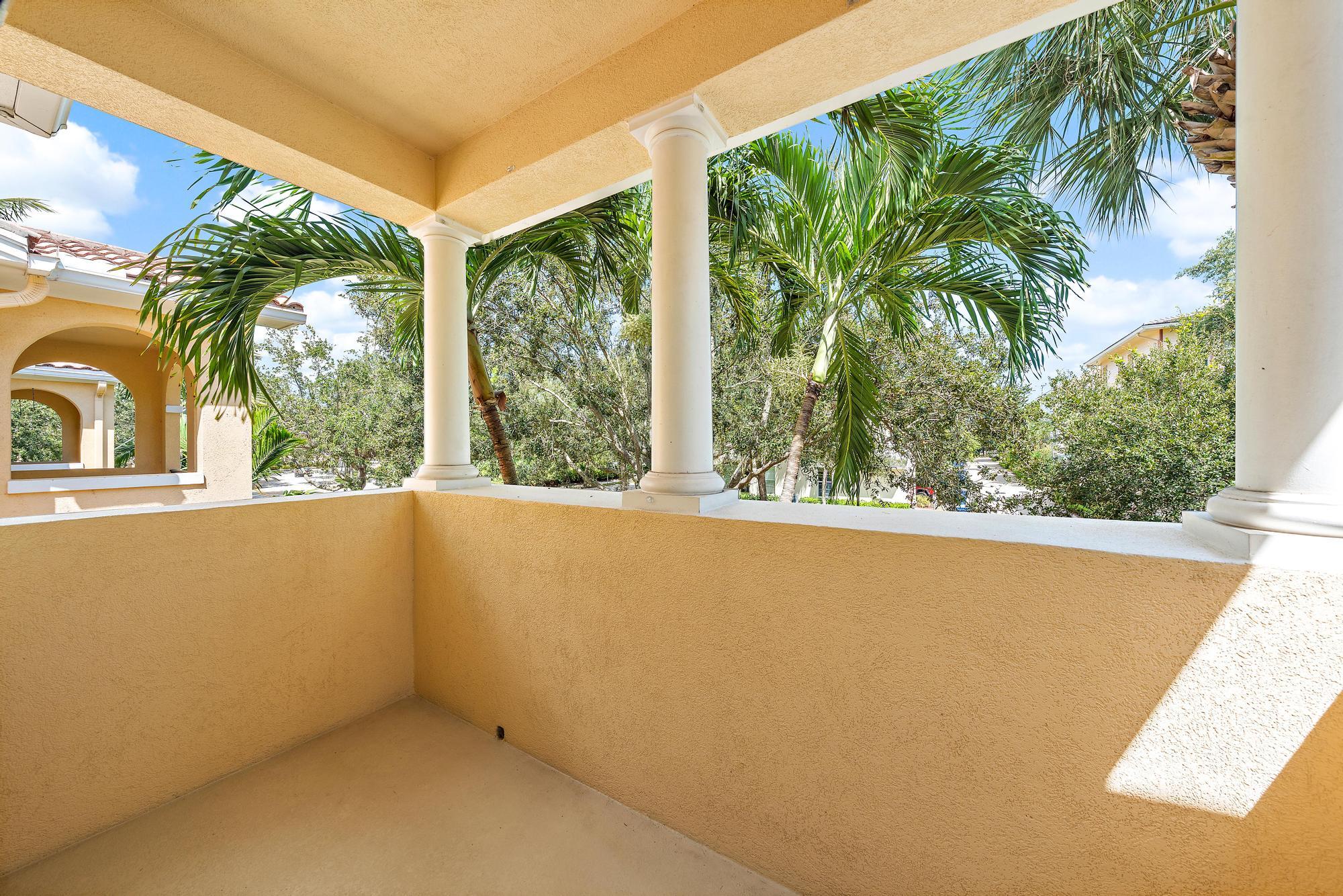 Covered balcony with white columns and palm trees beyond the railing.