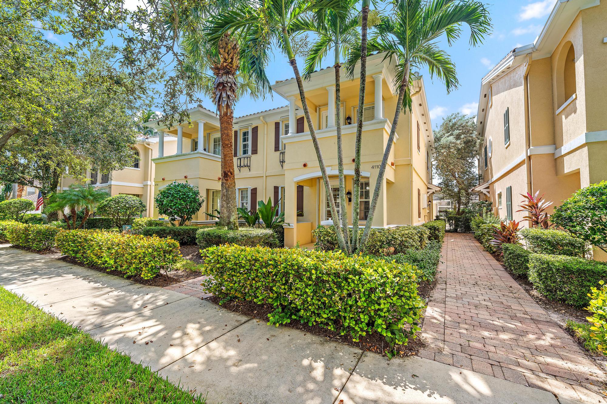 Yellow two-story home with white columns, palm trees, and a brick walkway.